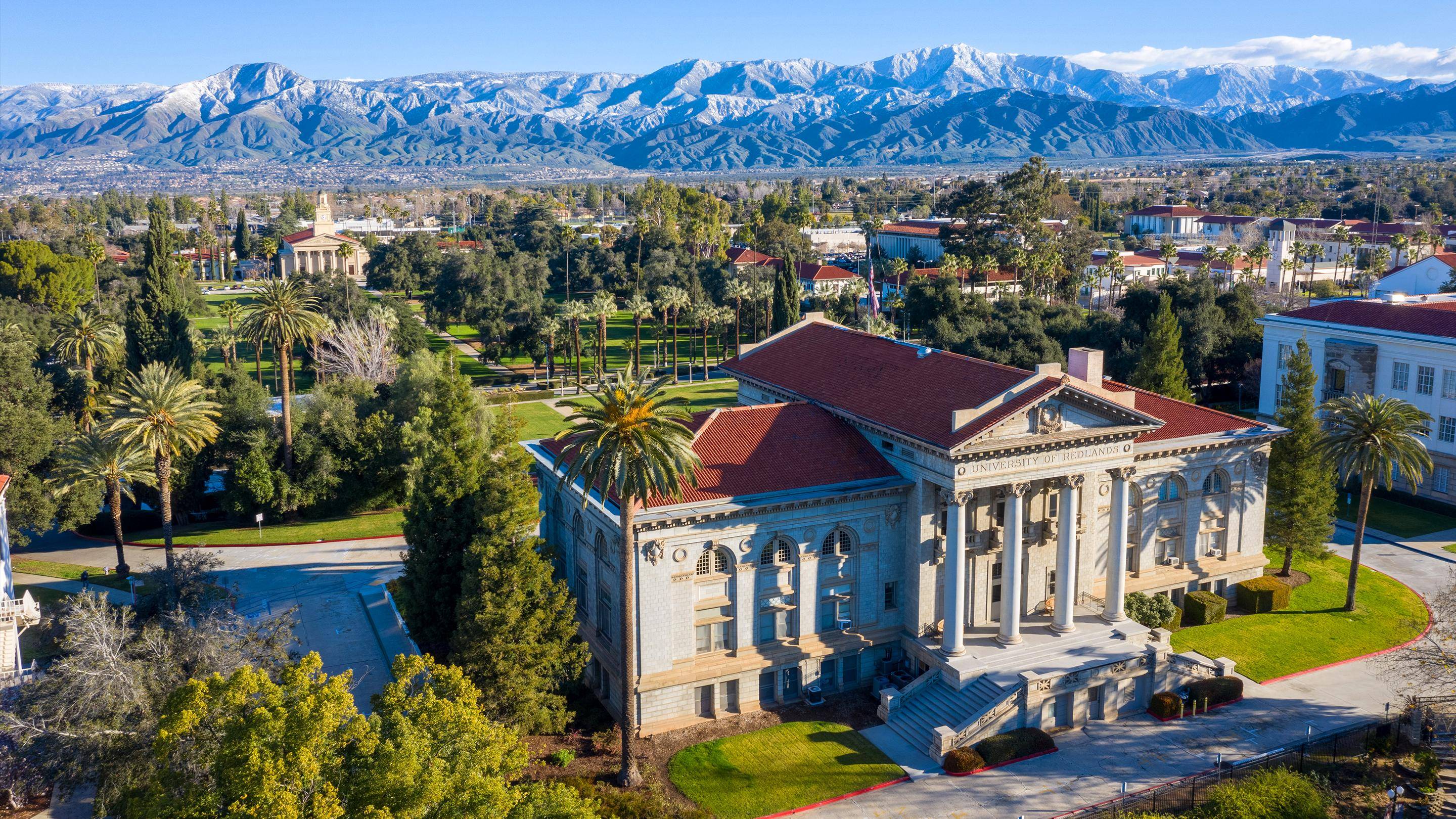 a building with columns and a lawn with trees and mountains in the background