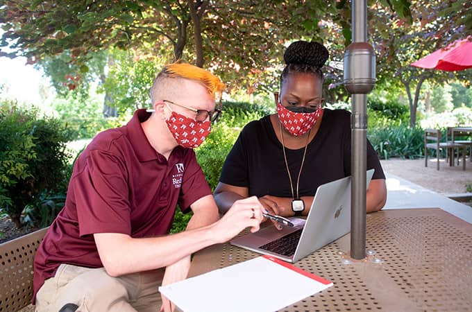 a person and person wearing face masks sitting at a table with a laptop
