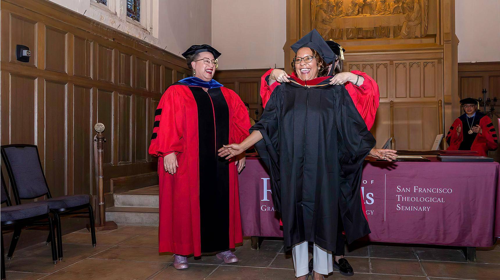 a person in a graduation gown and cap standing next to a person in a robe