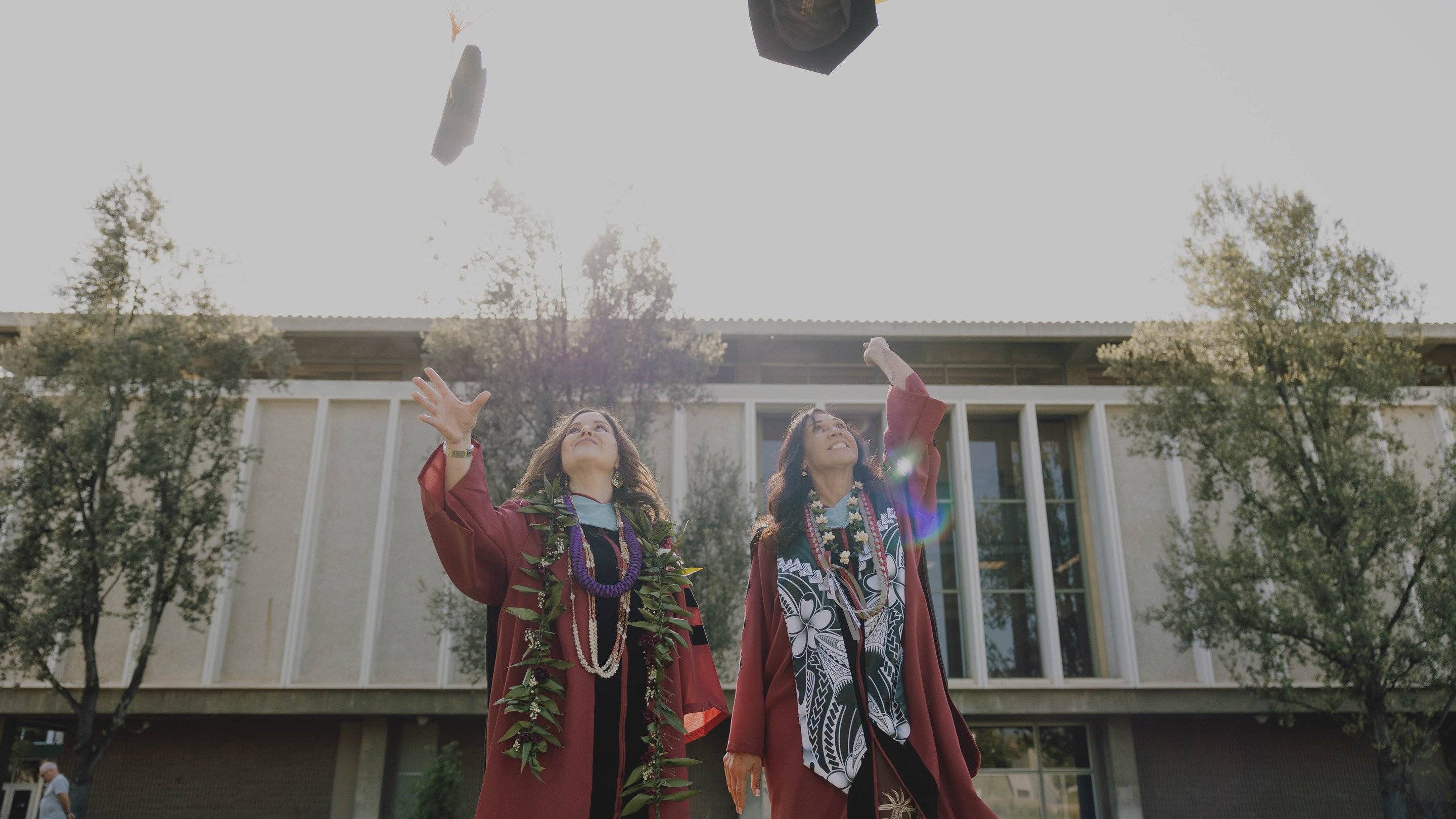 two women in graduation gowns throwing caps in the air
