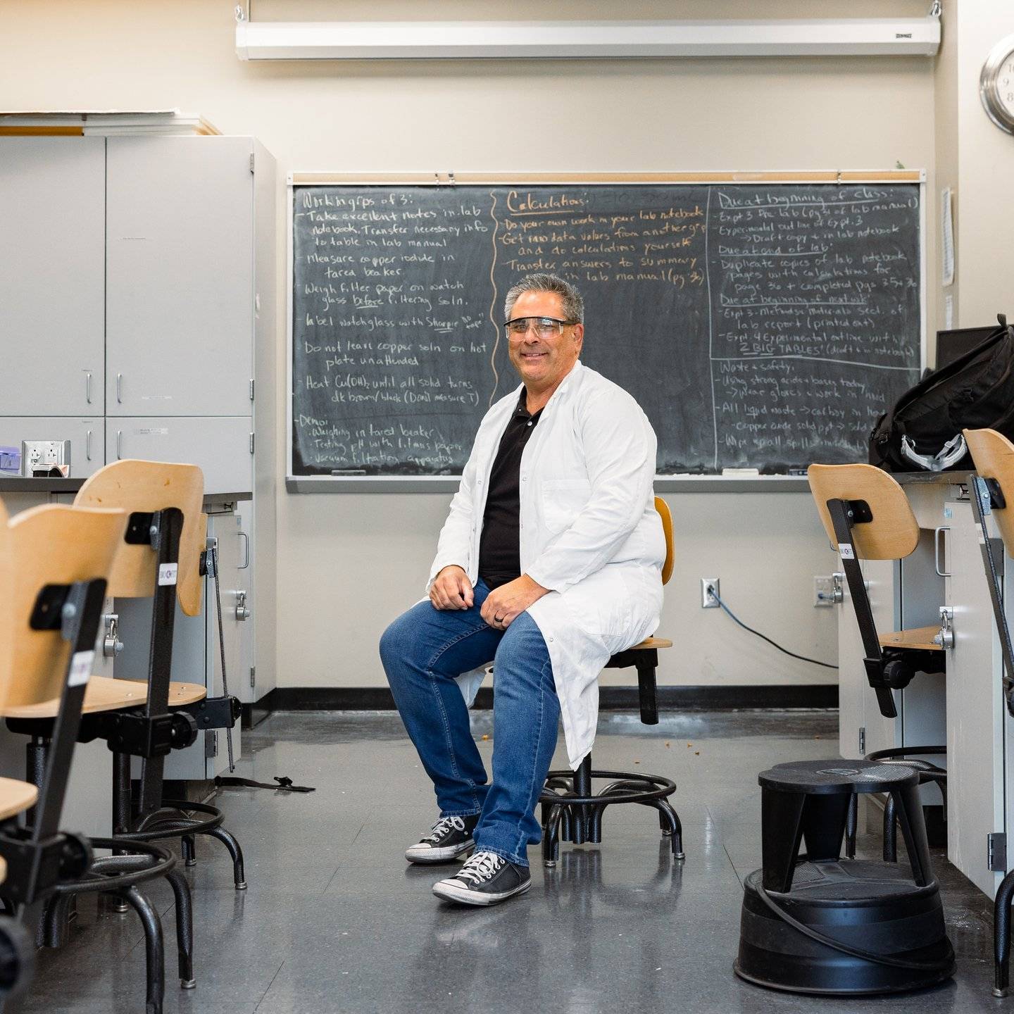 a person in a white coat sitting in a chair in a classroom