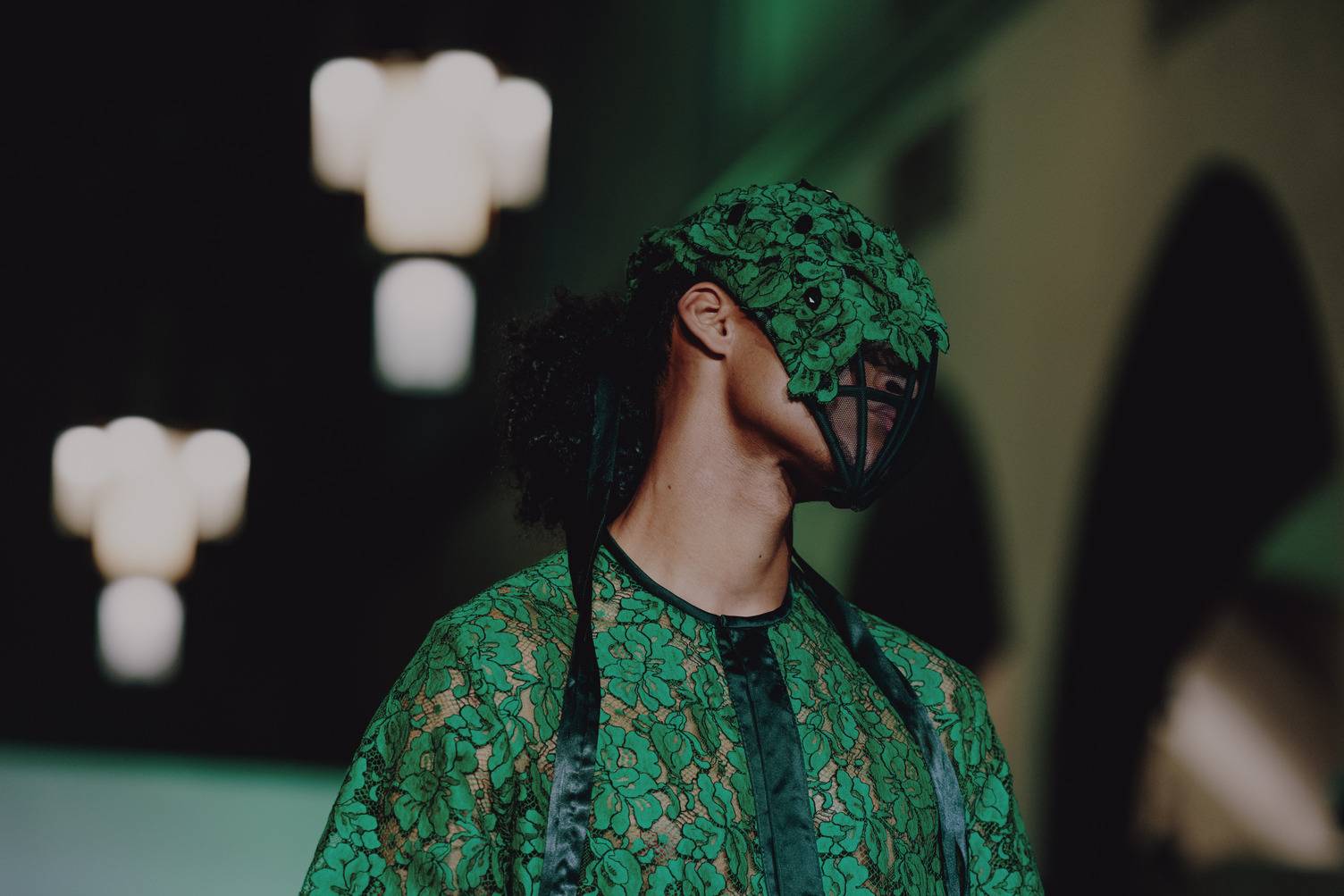 a person wearing a green lace dress and a mask