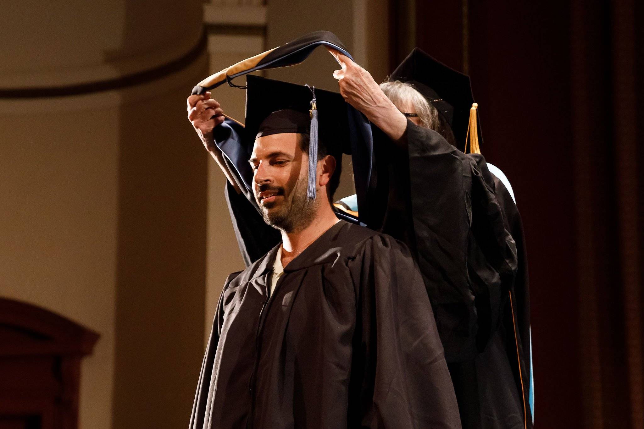 a person in a graduation gown holding a cap on his head
