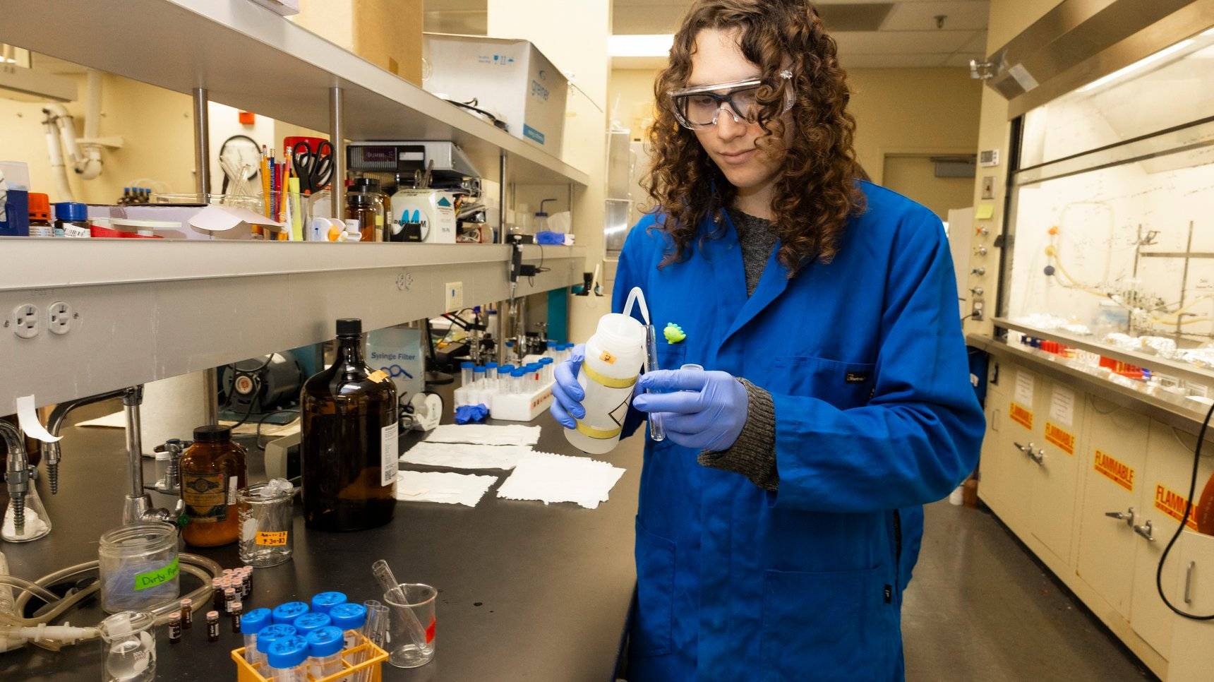 a person wearing blue lab coat and gloves holding a container