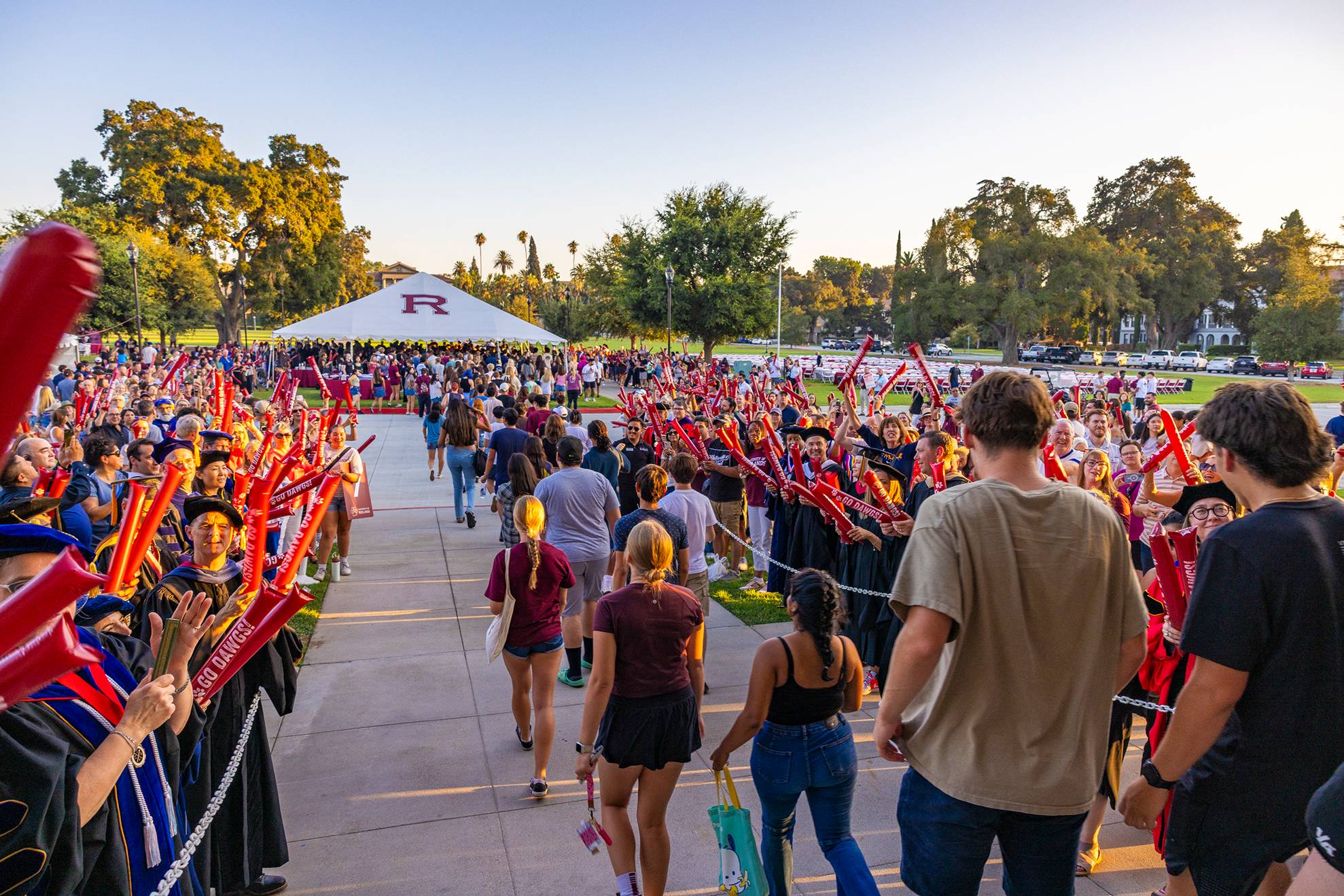 a group of people walking on a sidewalk with a white tent