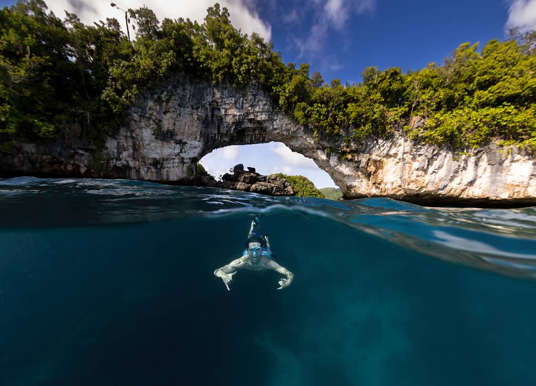 a person swimming under a rock arch