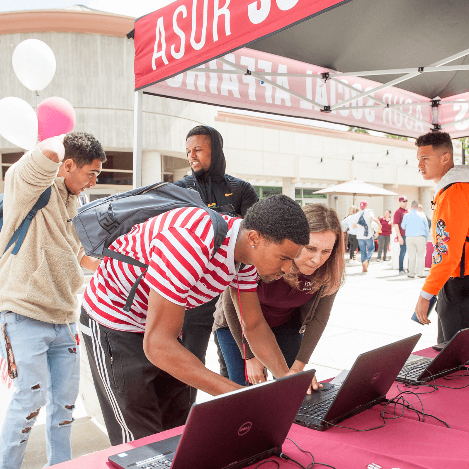 a group of people standing around a table with laptops