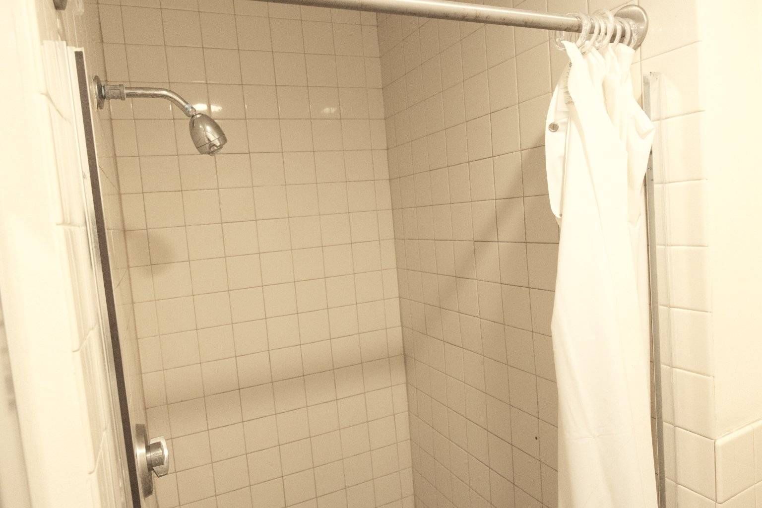 a shower with a shower head and a white shower curtain