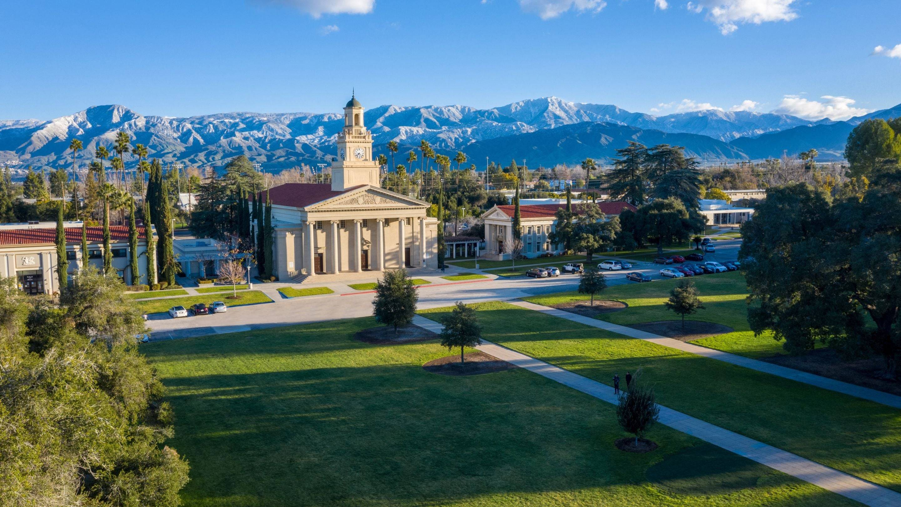 a building with a tower and a lawn with trees and mountains in the background