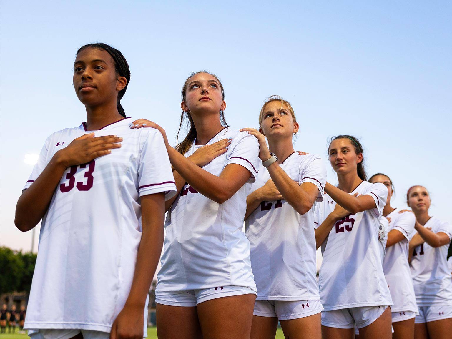 a group of women in white uniforms standing in a line with their hands on their chest