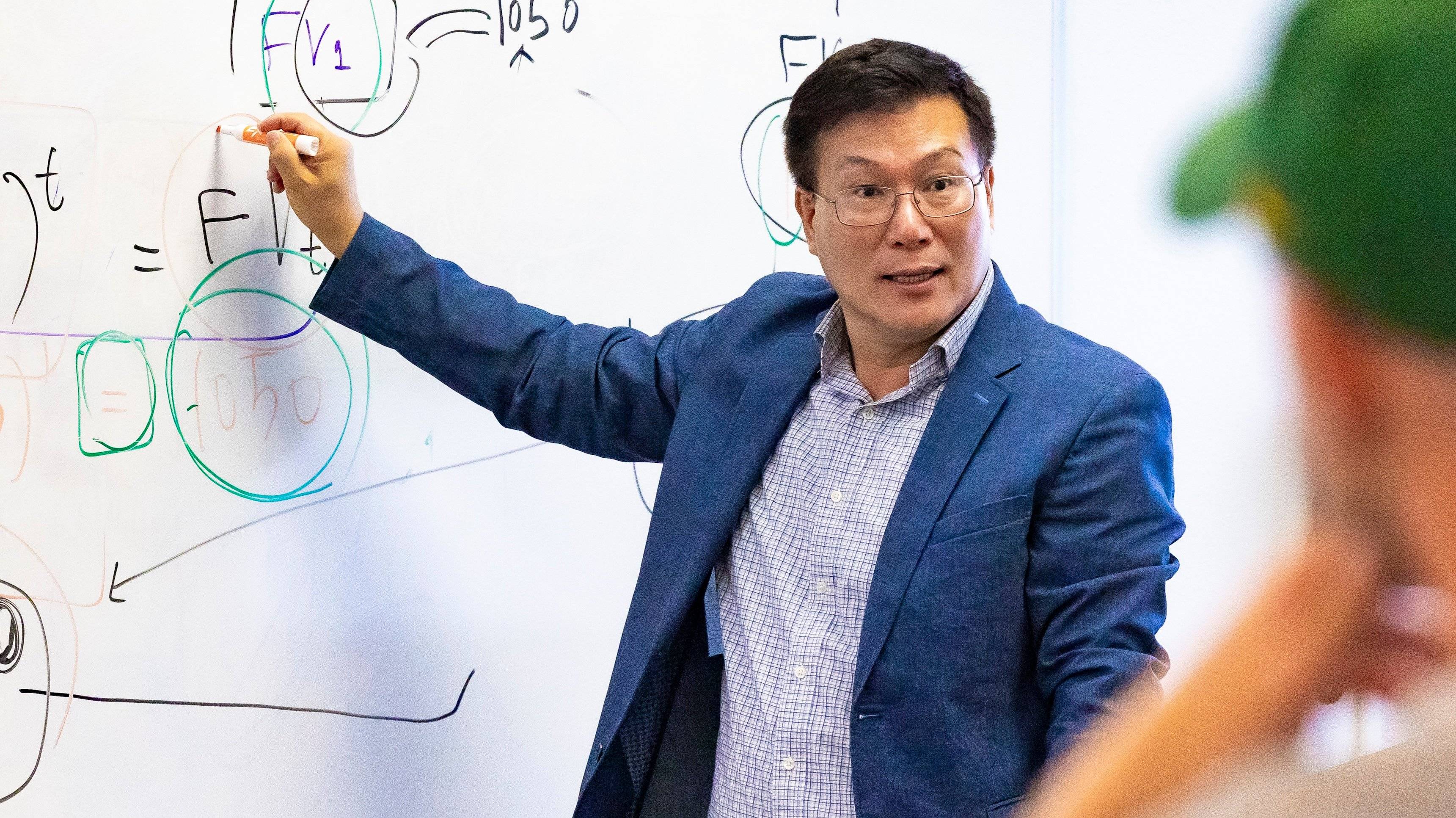 a person in a suit pointing at a whiteboard