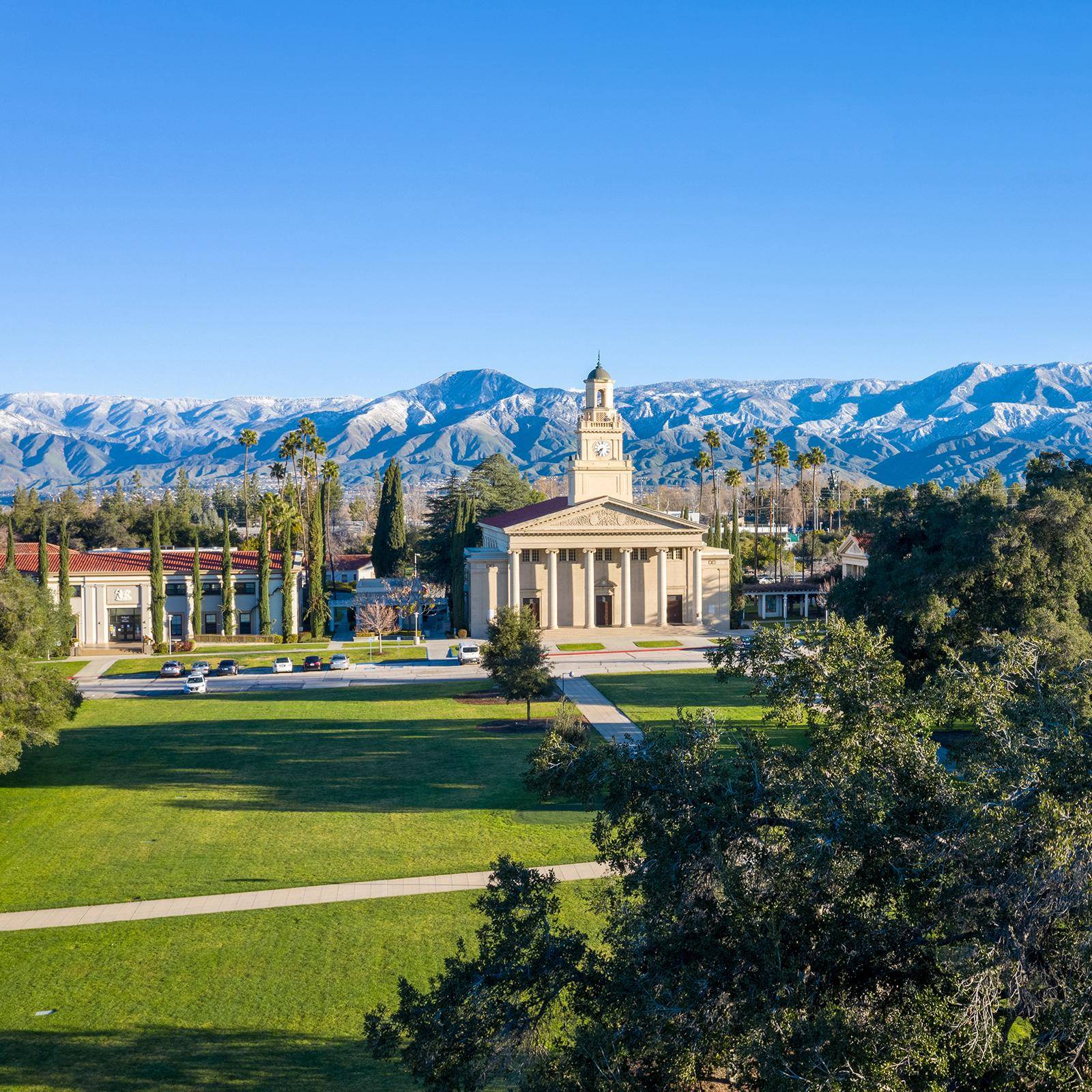 a building with a tower and a lawn with trees and mountains in the background