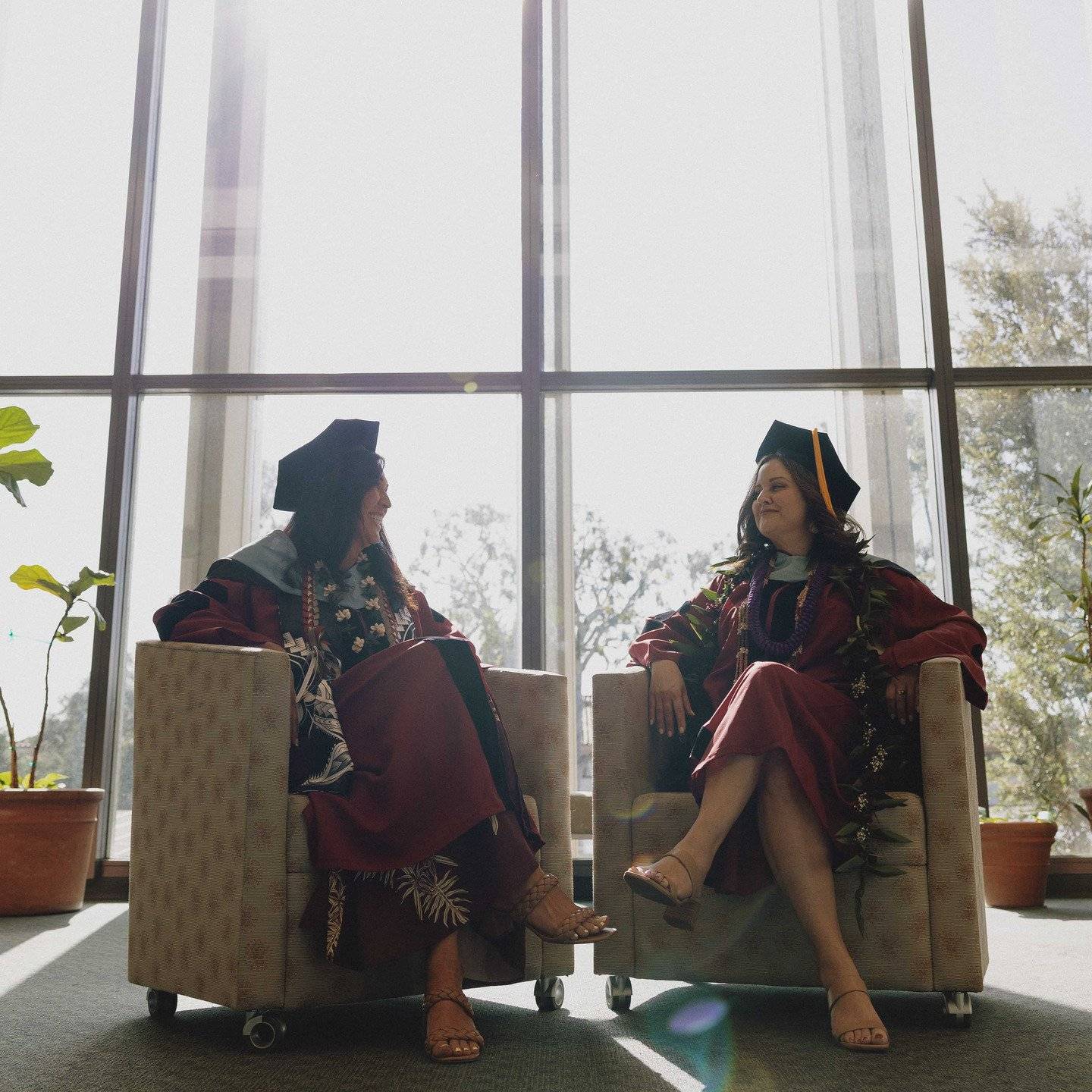 two women in graduation gowns and caps sitting in chairs