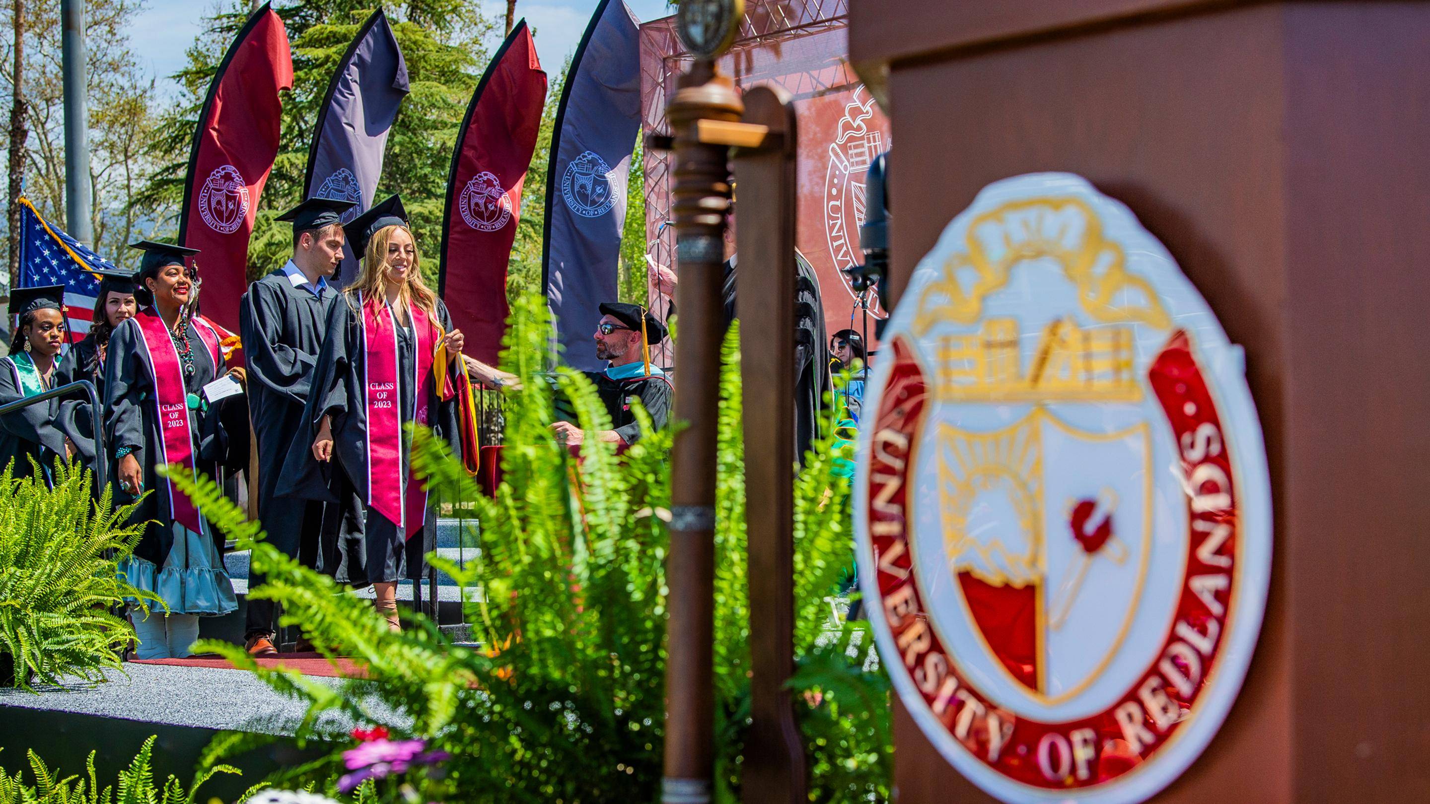 a group of people in graduation gowns and caps walking in front of flags