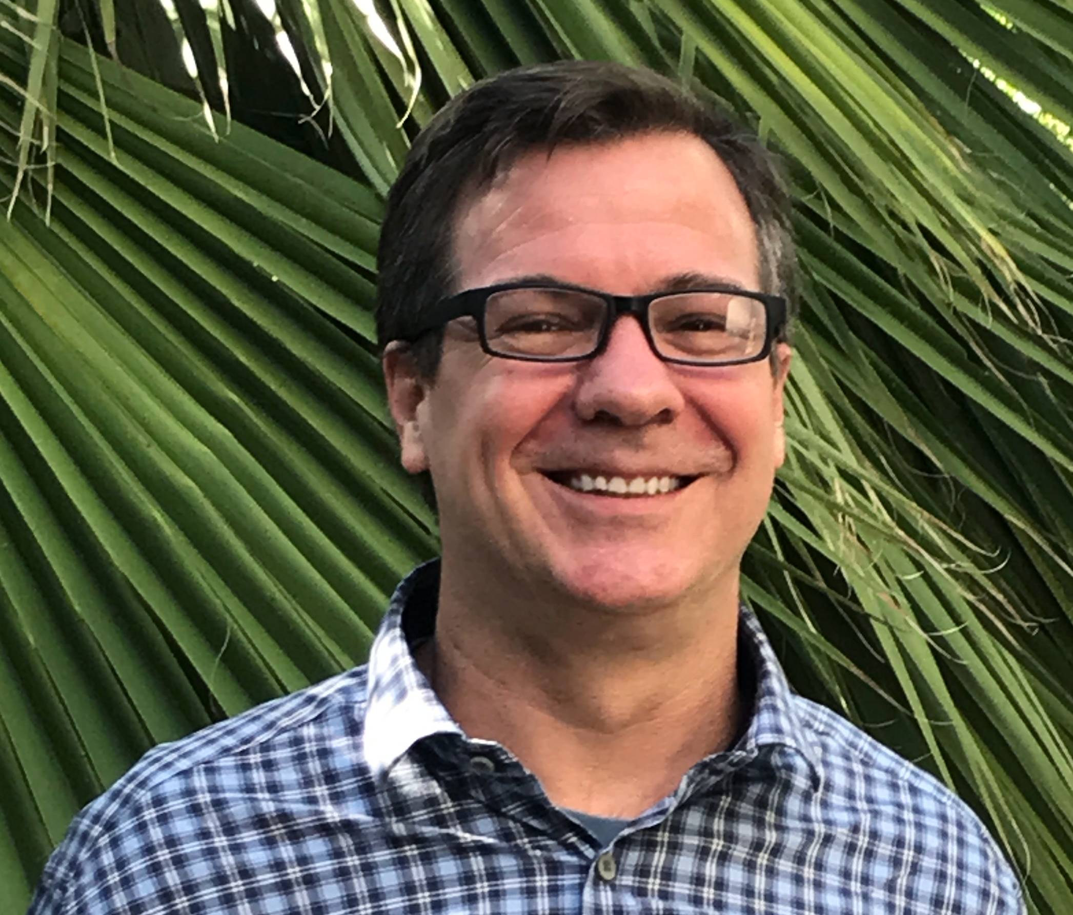 a person smiling in front of a palm tree