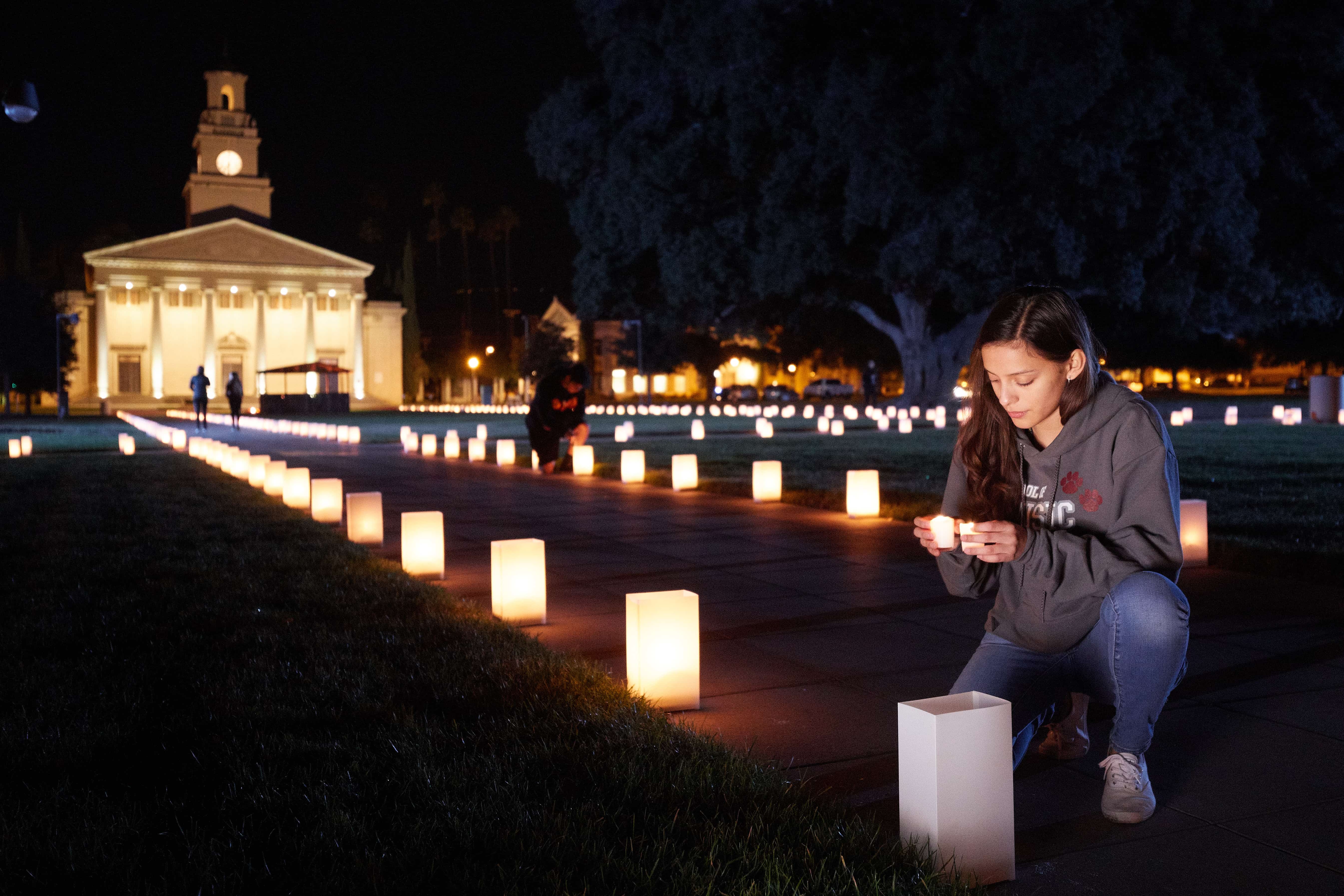 a person kneeling on a sidewalk with a lit up candle in the middle
