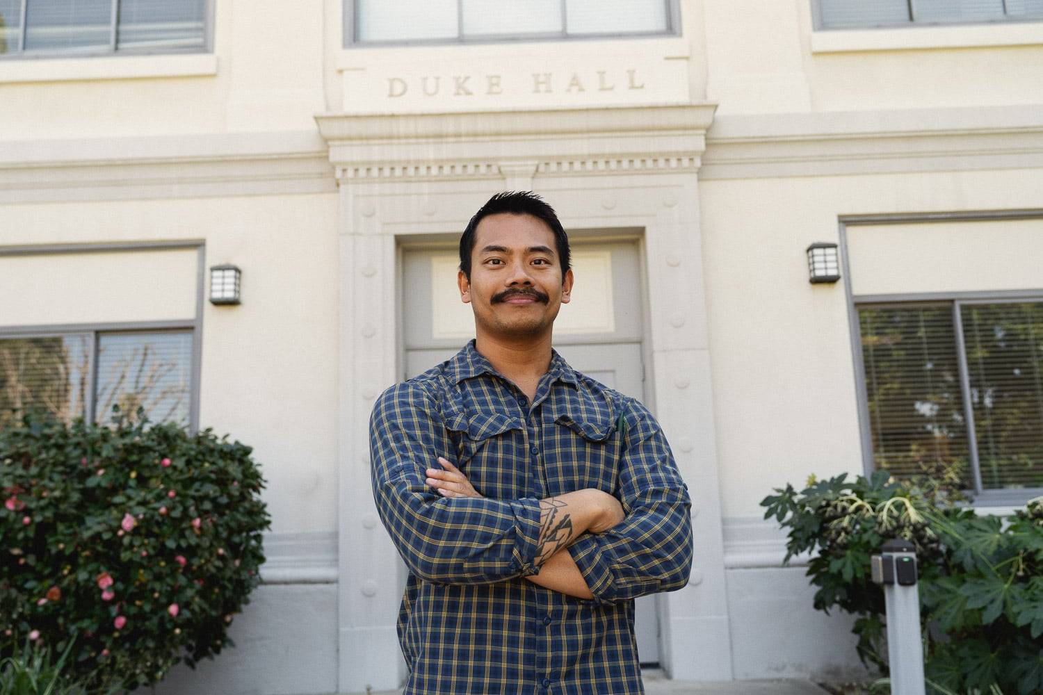 a person with mustache and crossed arms in front of a building