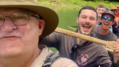 a person in a hat and glasses with a stick in front of a person in a boat