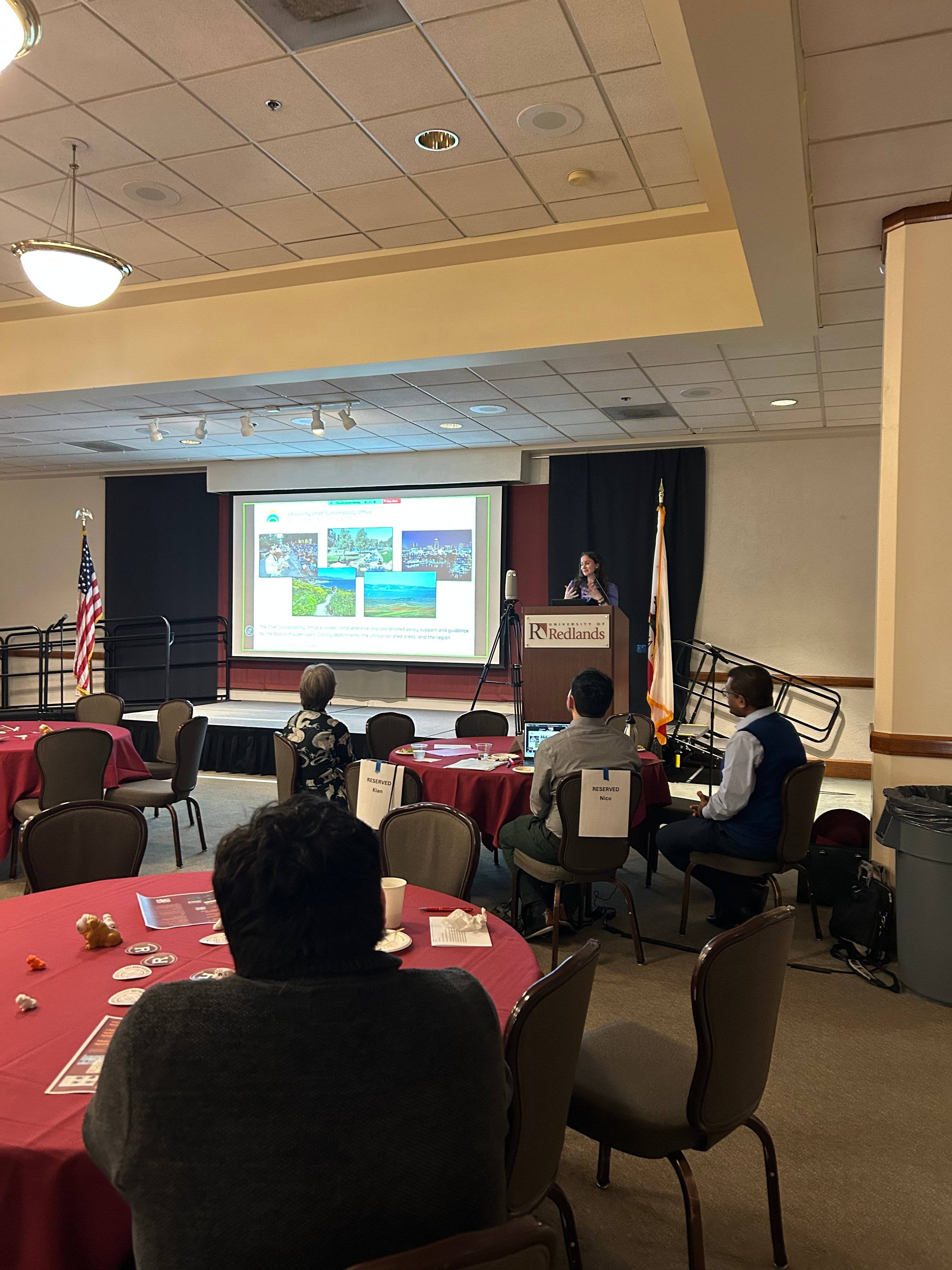 a group of people sitting around tables and a projector screen