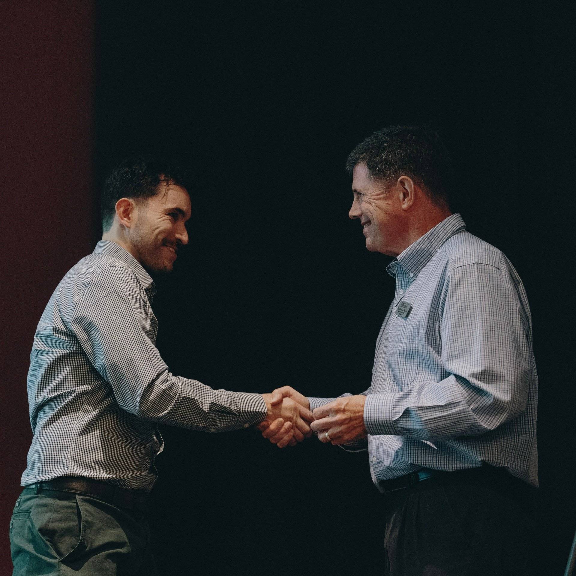 two men shaking hands in front of a black background