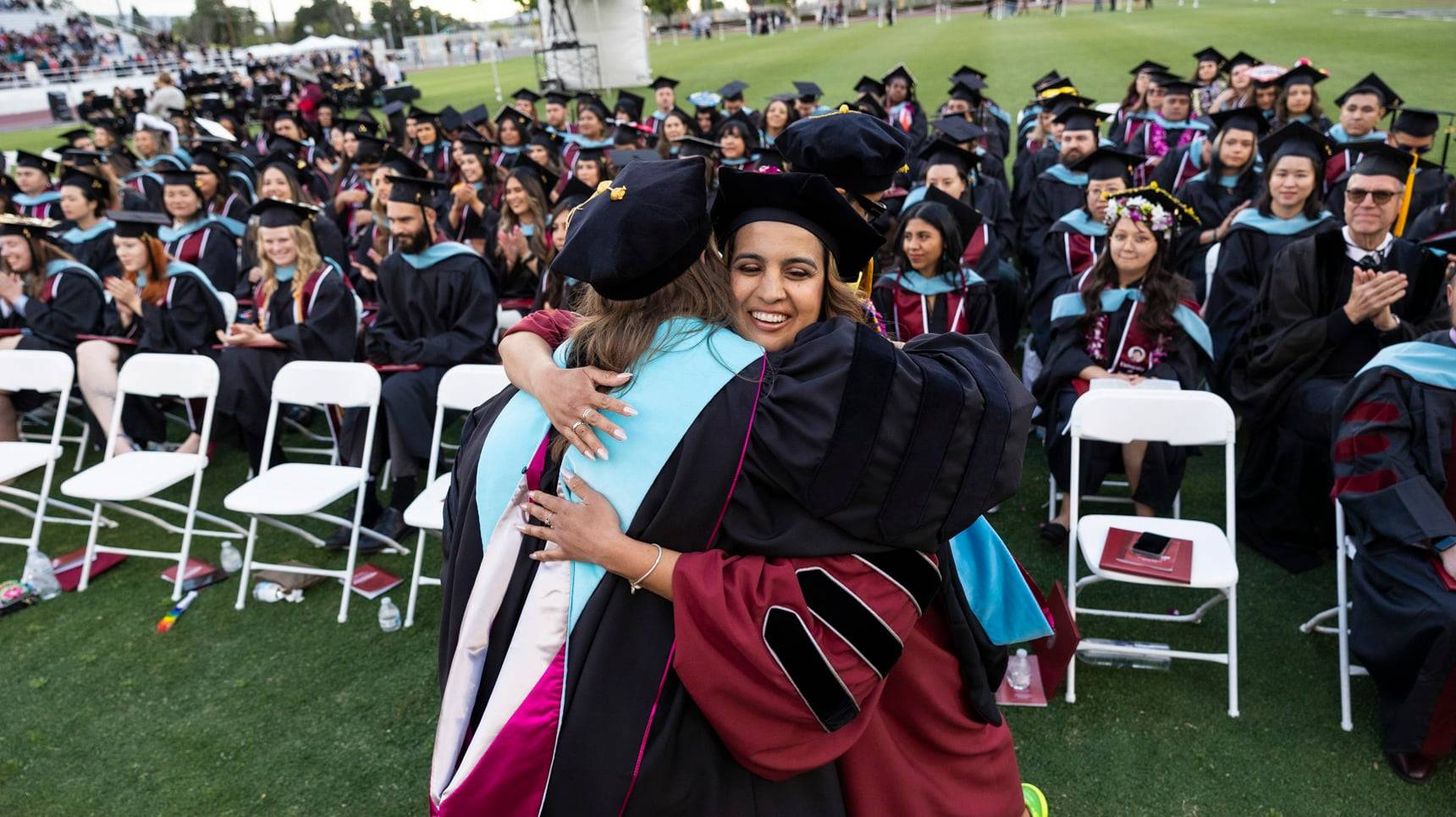 a person hugging another person in graduation gowns