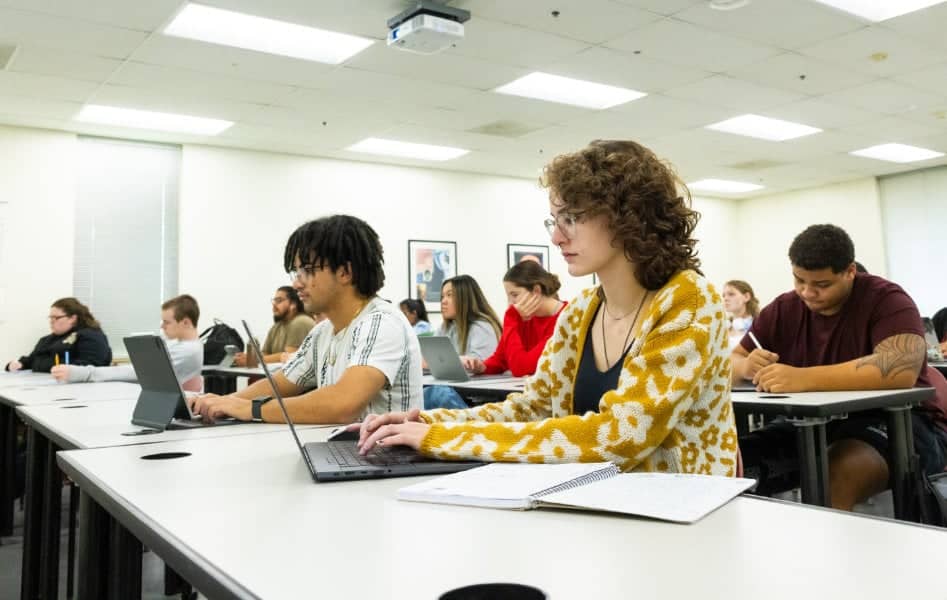 a group of people sitting at desks with laptops
