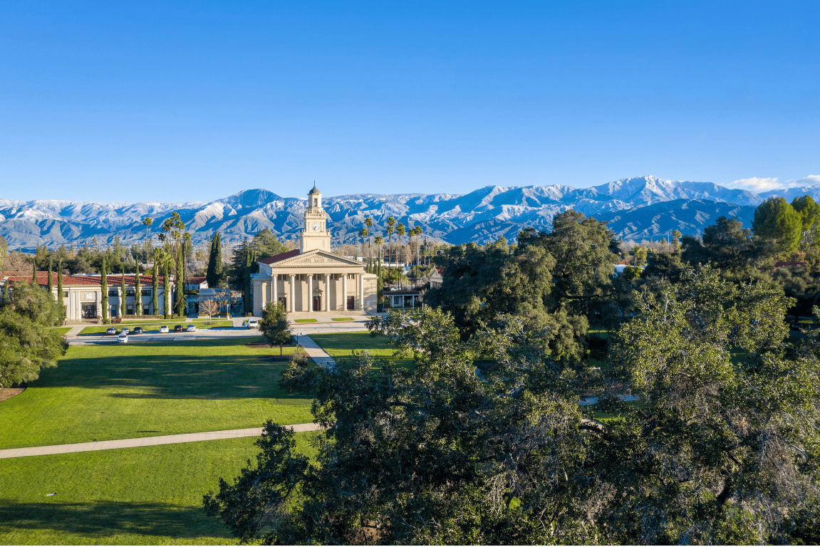 a building with a tower and a lawn with trees and mountains in the background