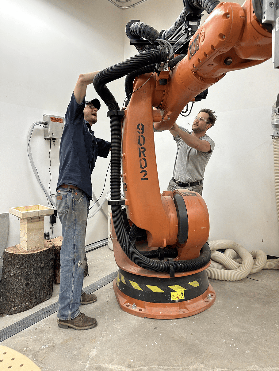 two men working on a large orange robotic arm