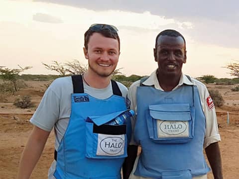 two men wearing blue vests standing in a desert