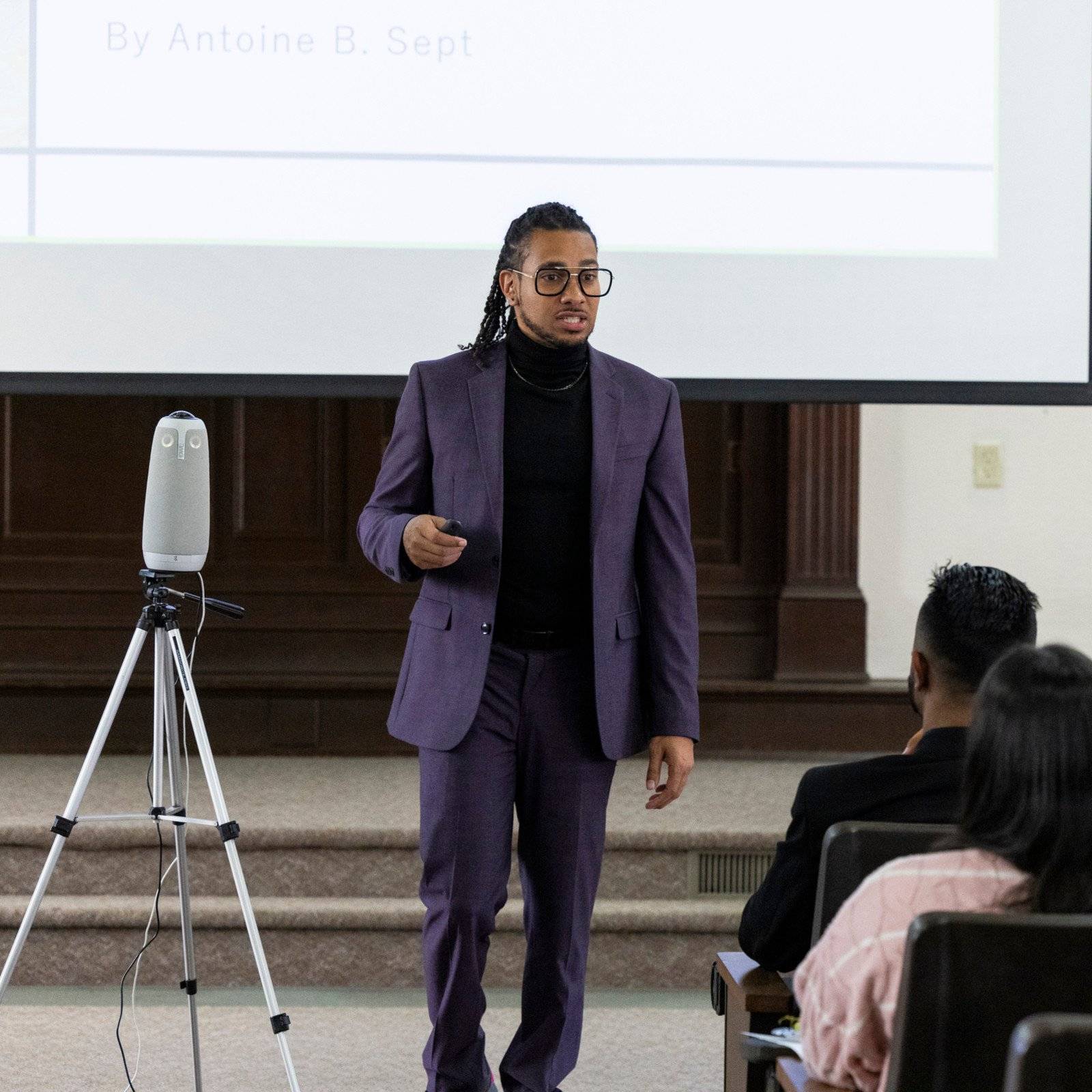 a person in a suit standing in front of a projector screen
