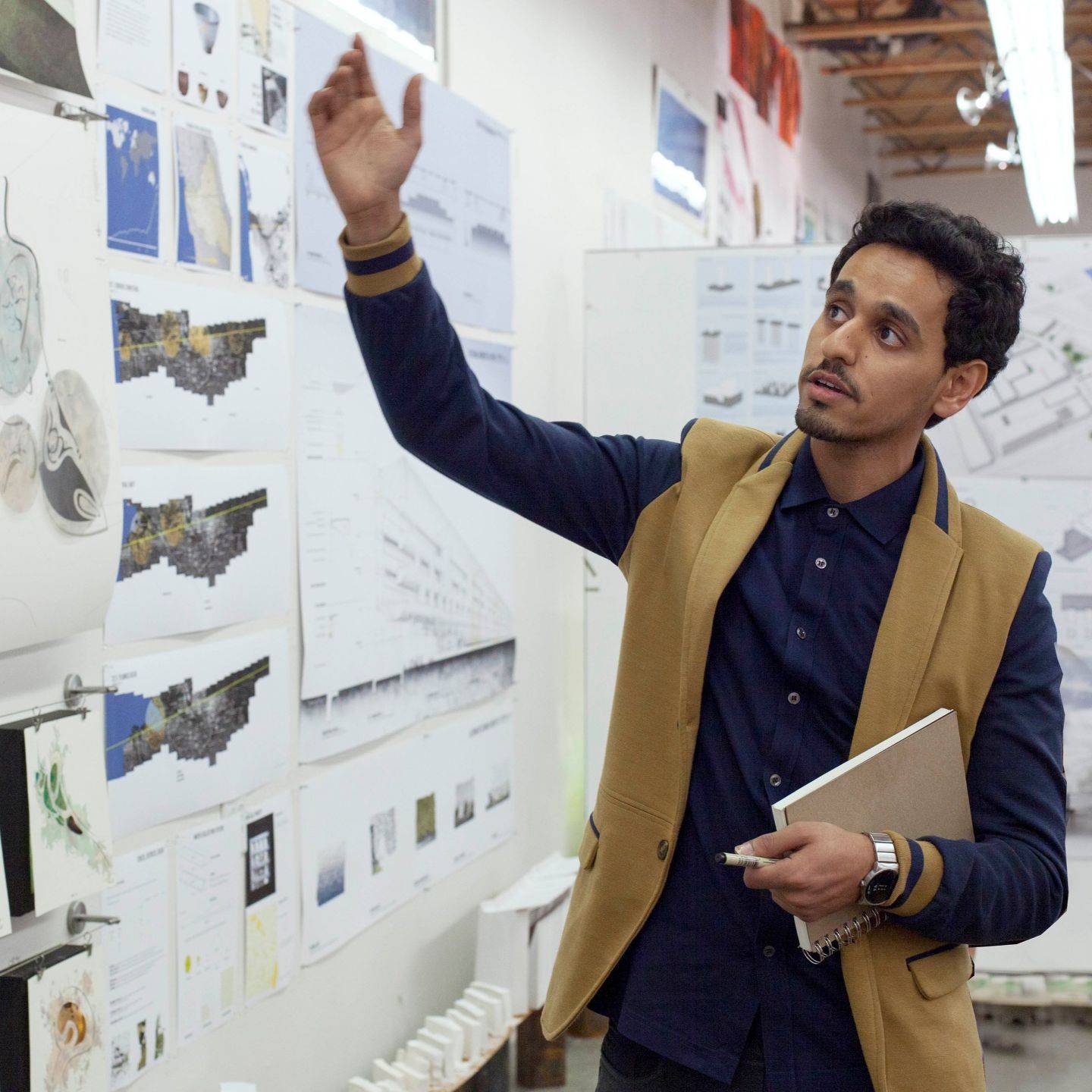 a person in a vest holding a notebook and looking at a wall with drawings