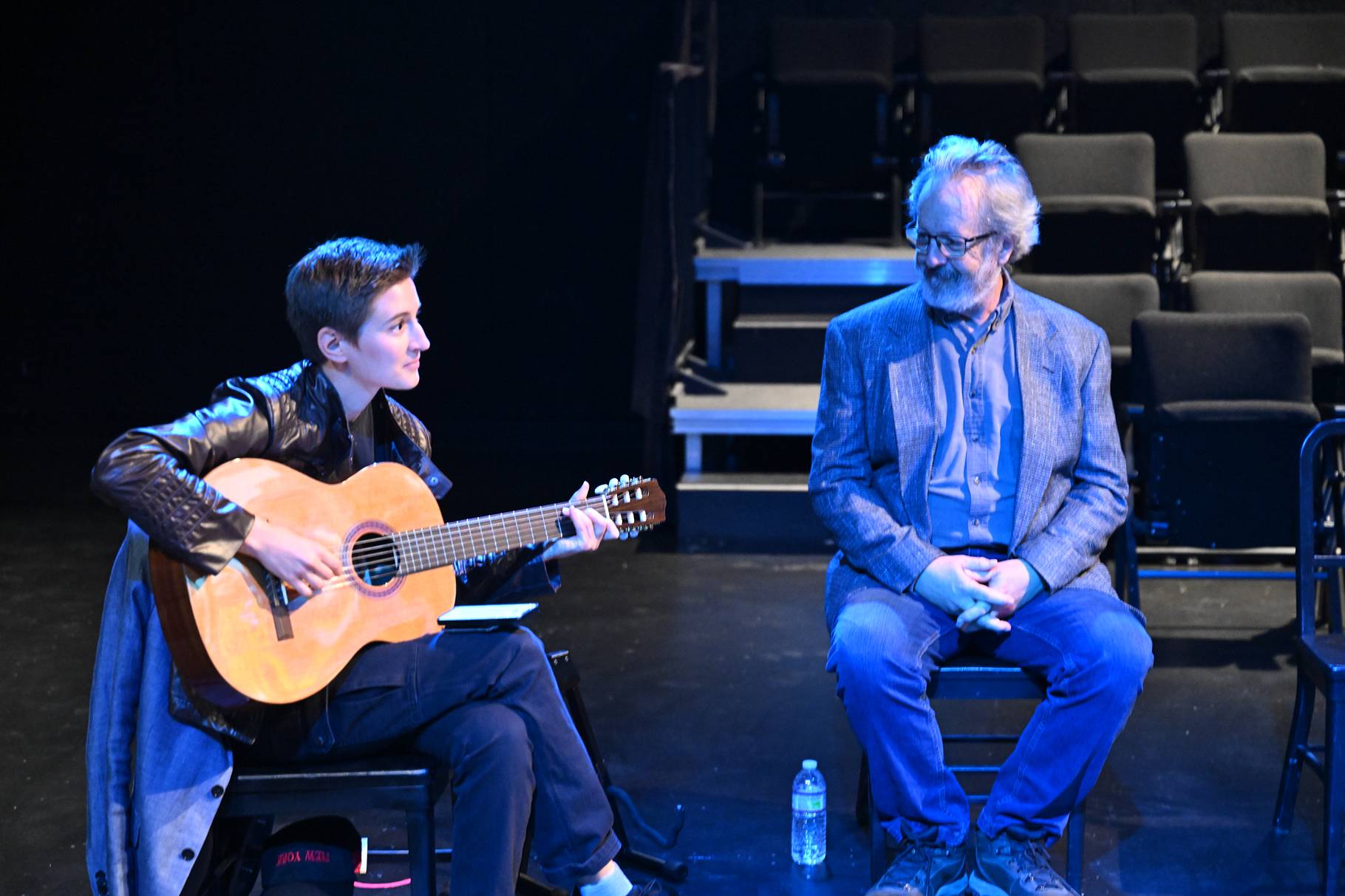 a person playing guitar next to a person sitting on a stage