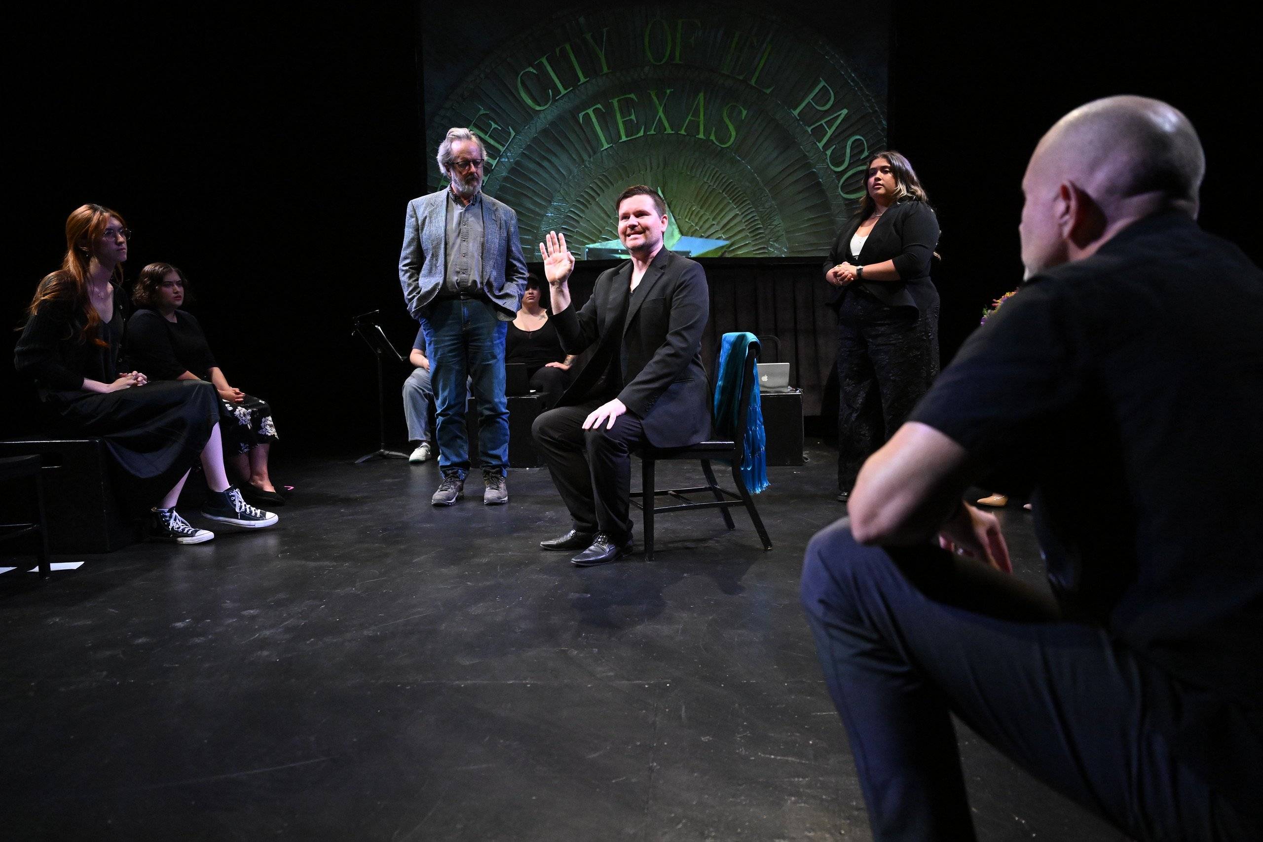 a person sitting in a chair on a stage with people watching