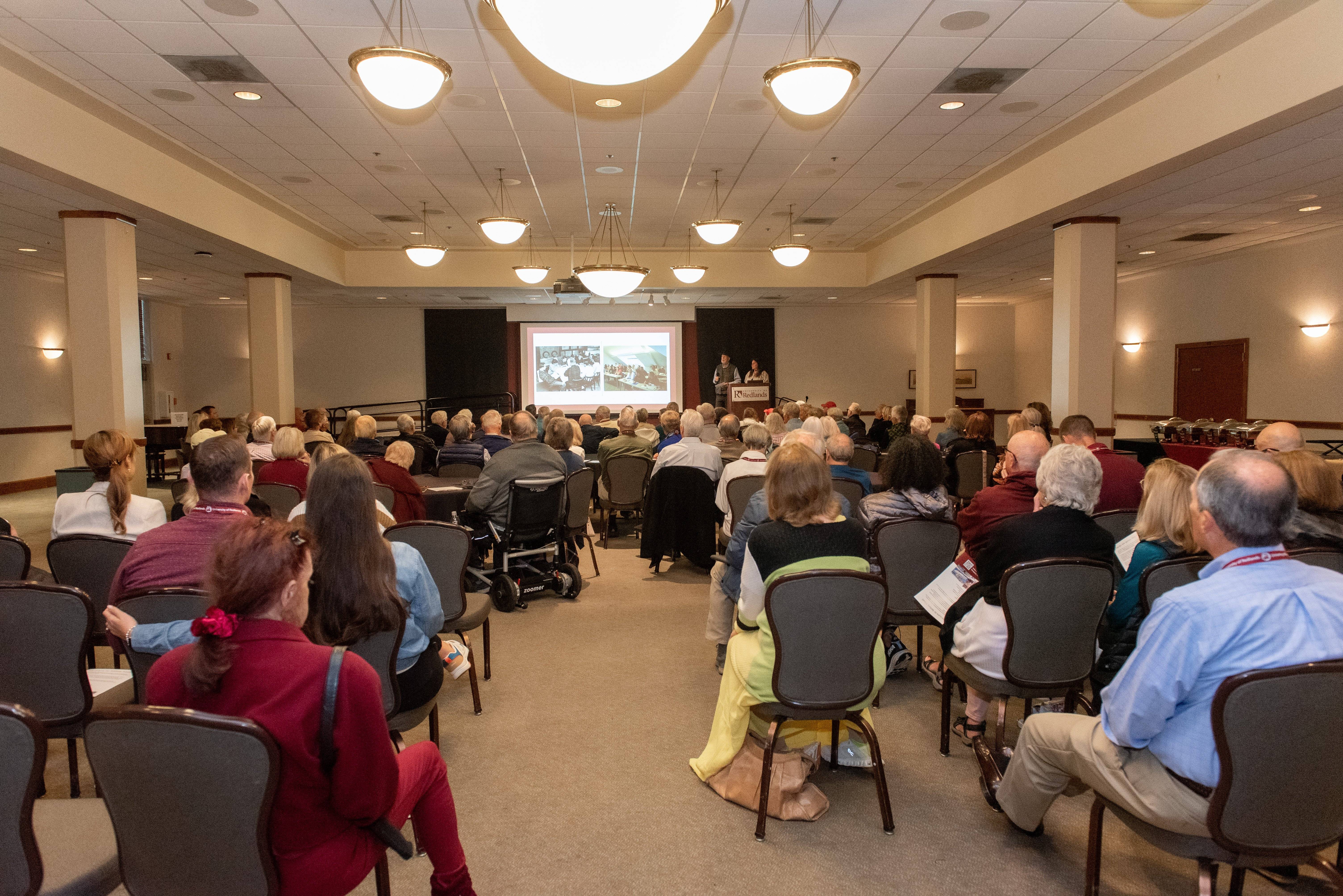 a group of people sitting in chairs in a room with a projection screen