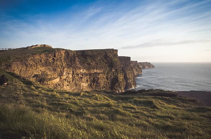 a cliff with grass and water in the background