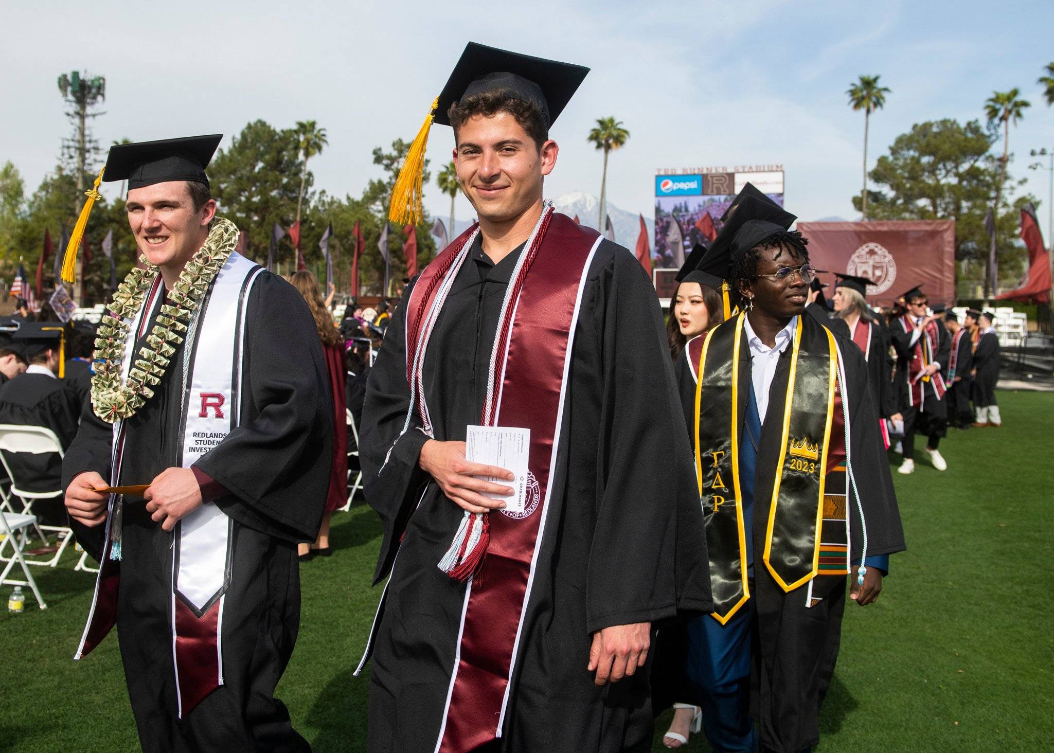 Student in cap and gown walking on the stadium lawn.