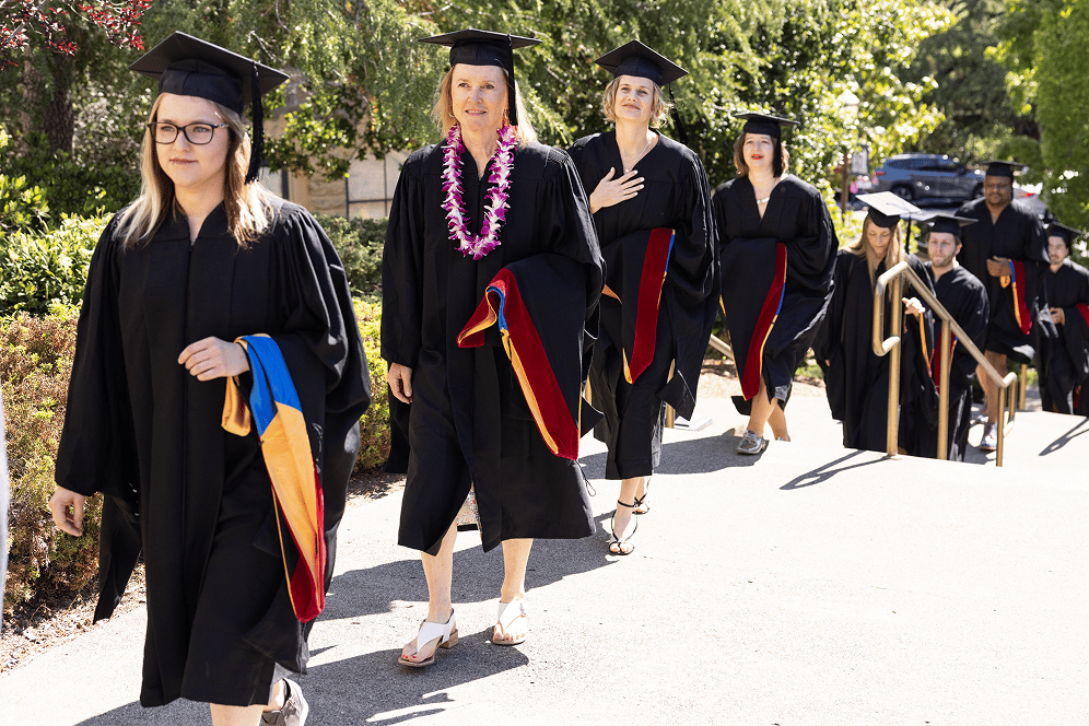 a group of women in graduation gowns and caps walking down a sidewalk