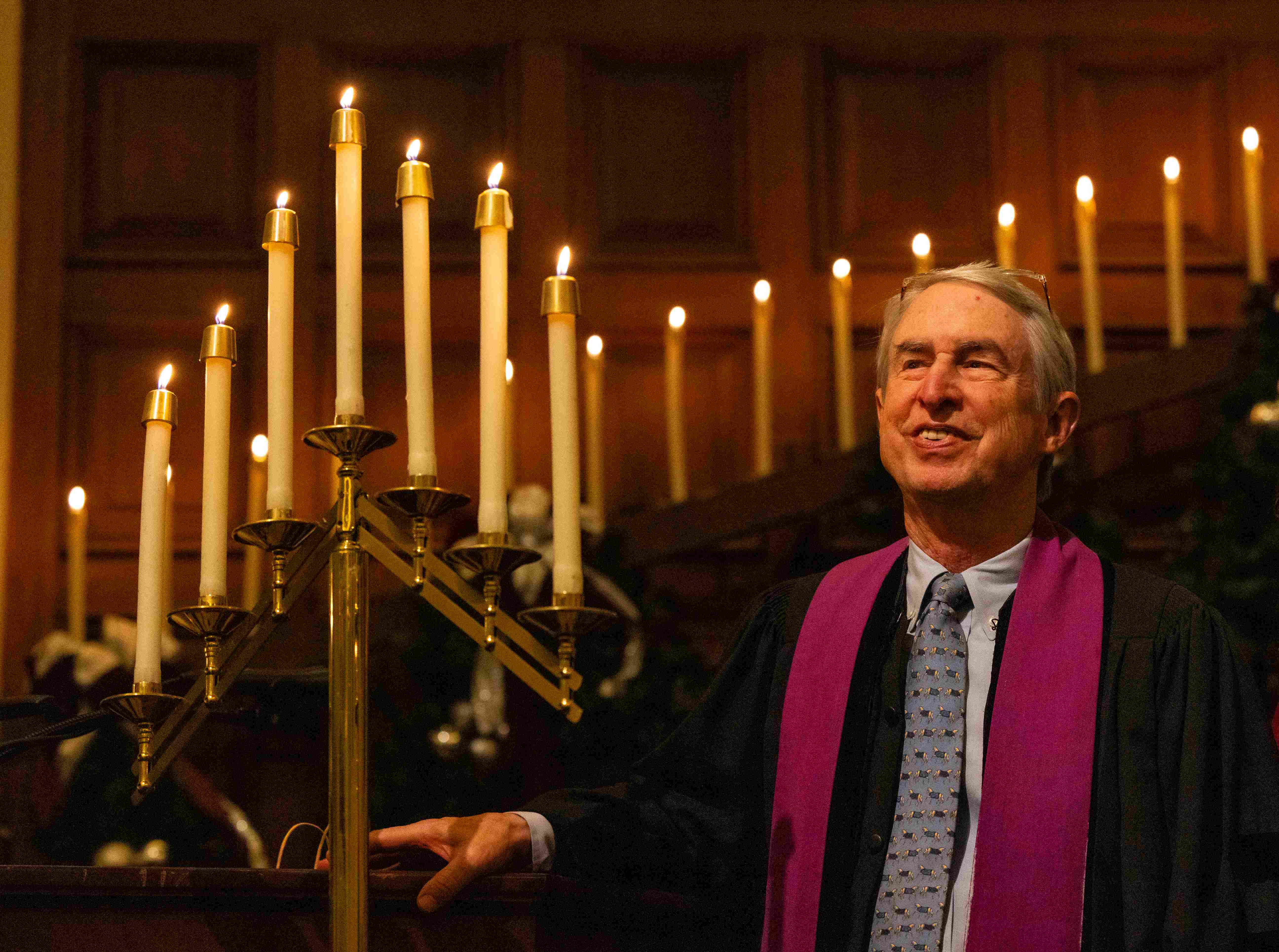 a person in a robe and tie standing next to a lit candle