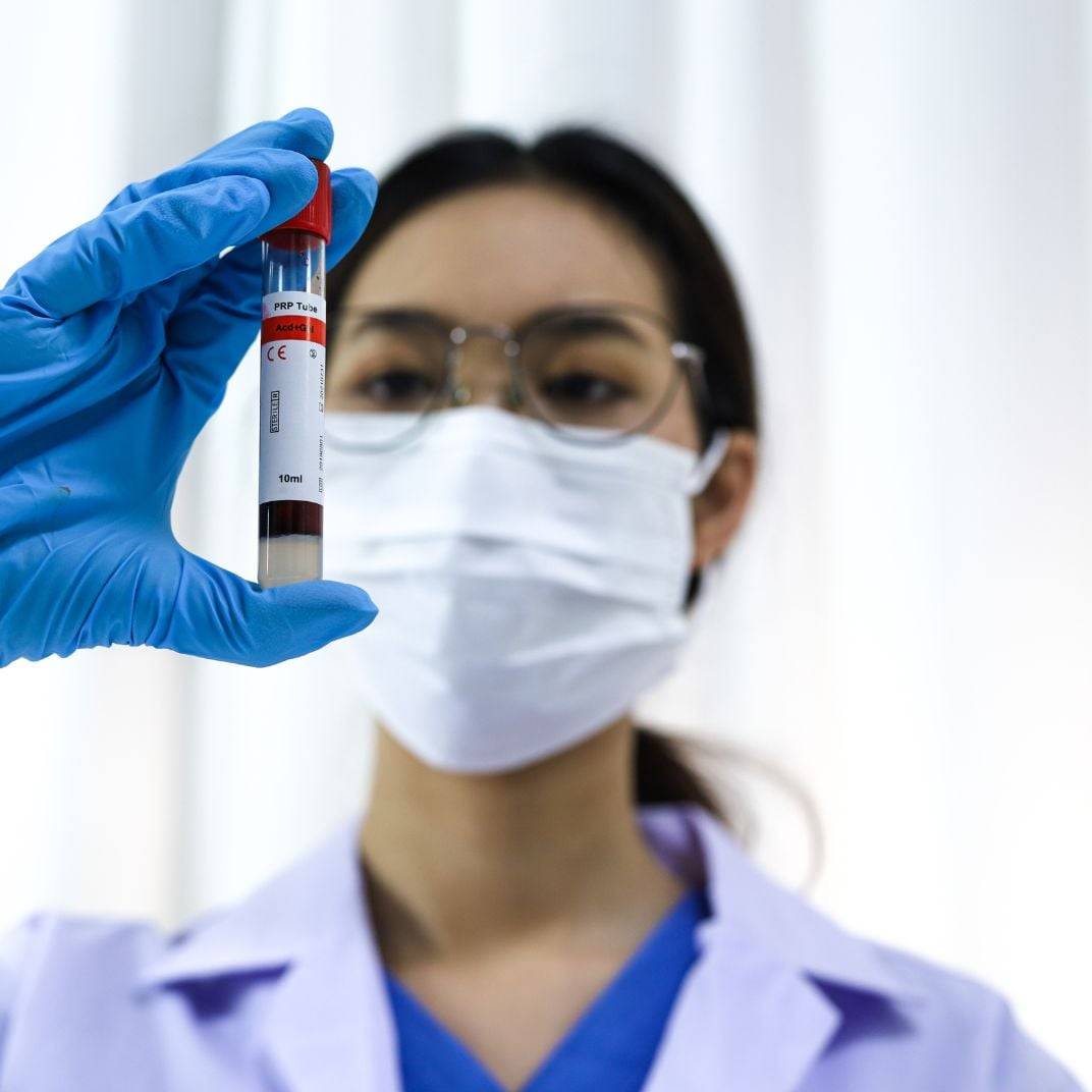 a person wearing a mask and gloves holding a tube of blood