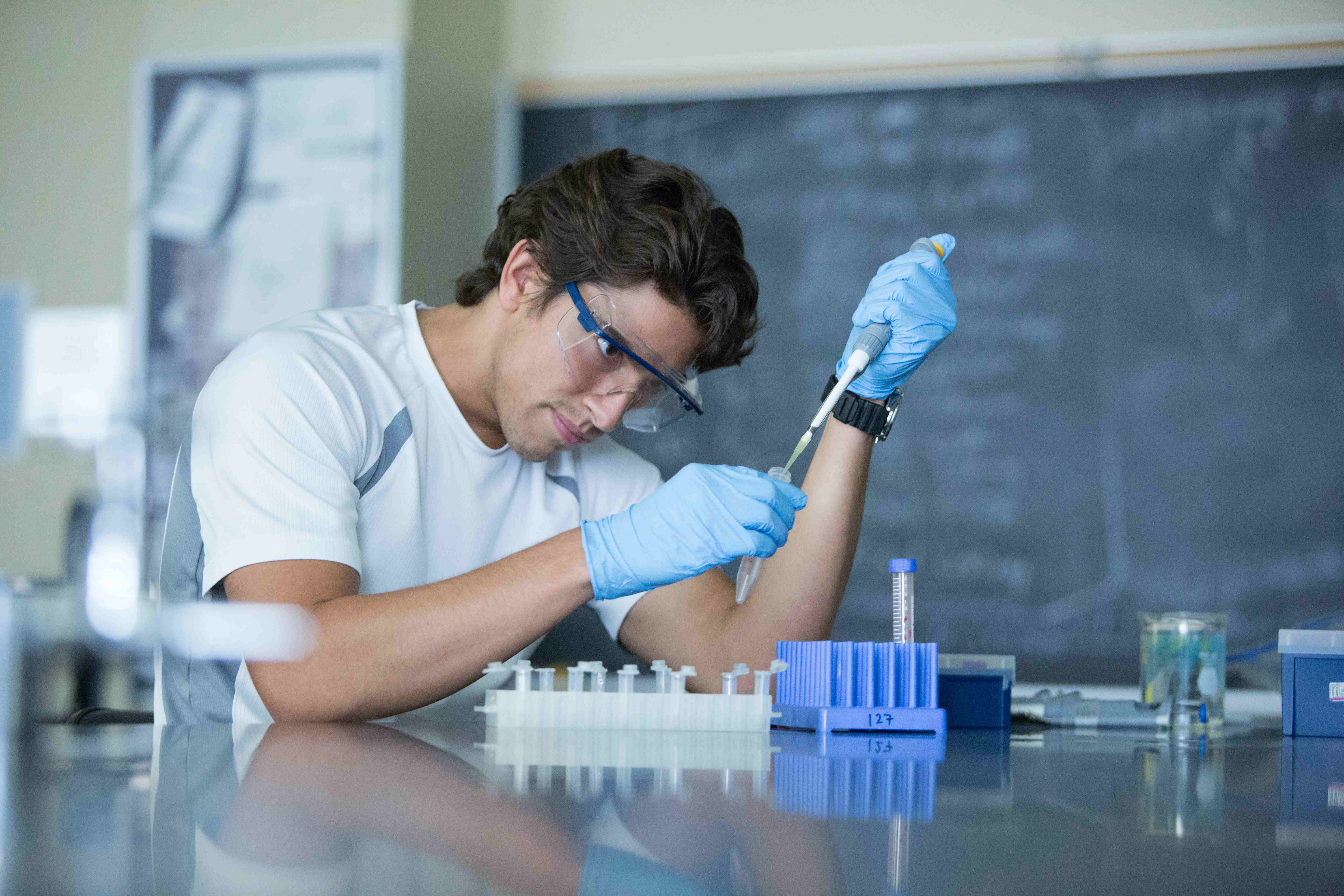 a person wearing goggles and gloves holding a pipette