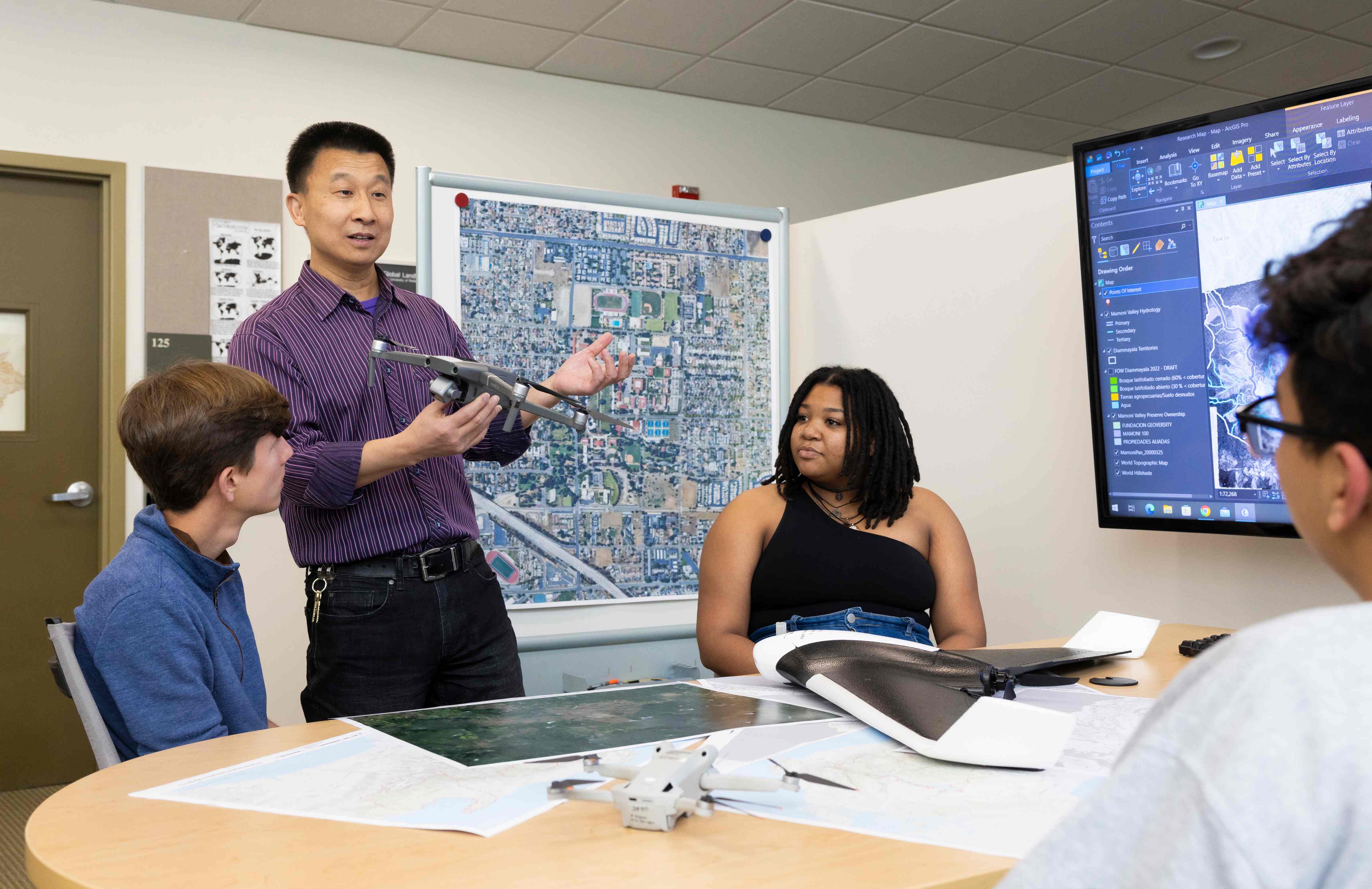 a person holding a drone and a person sitting at a table with a large screen