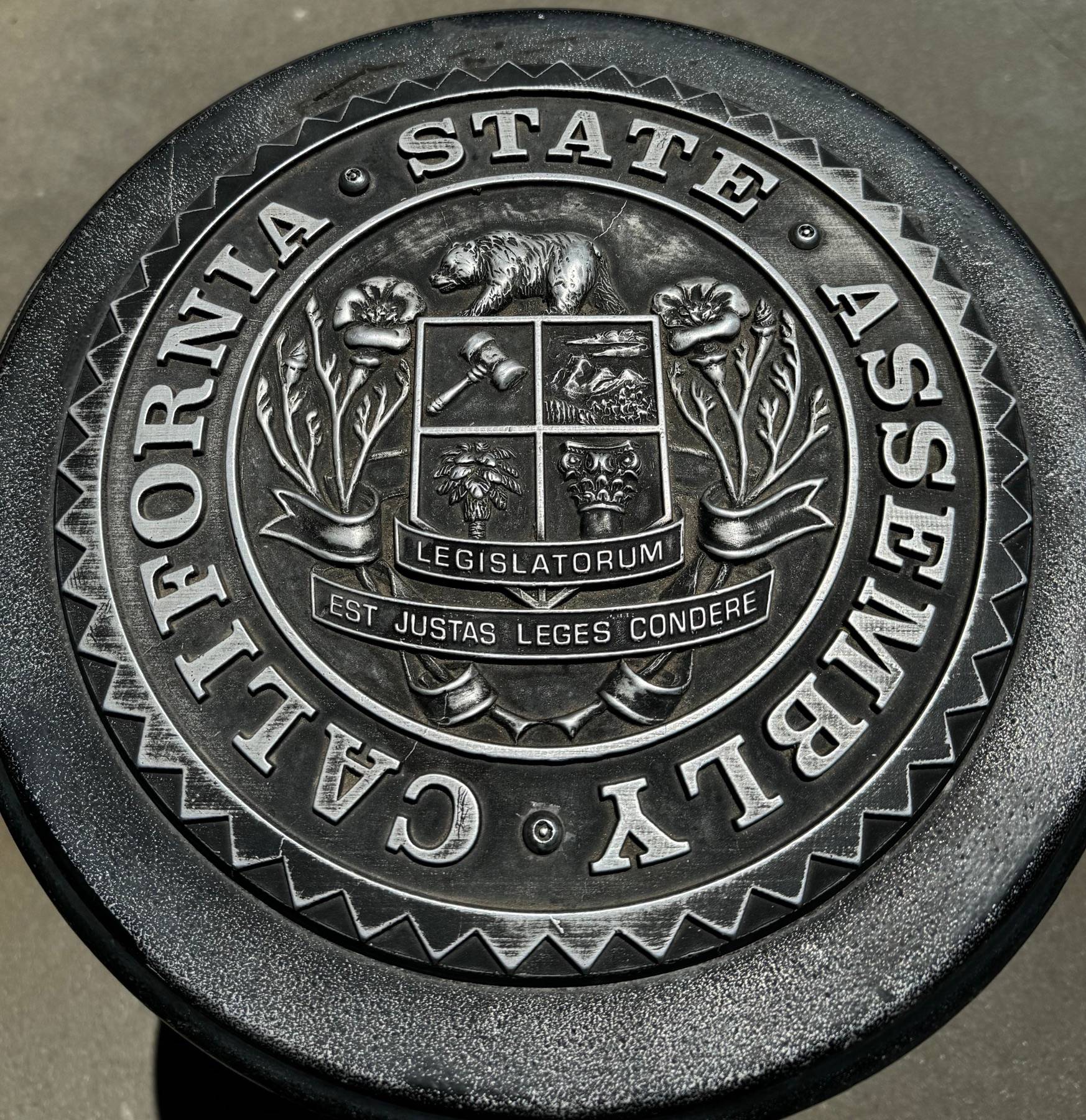 A circular metal California State Assembly seal with raised lettering.