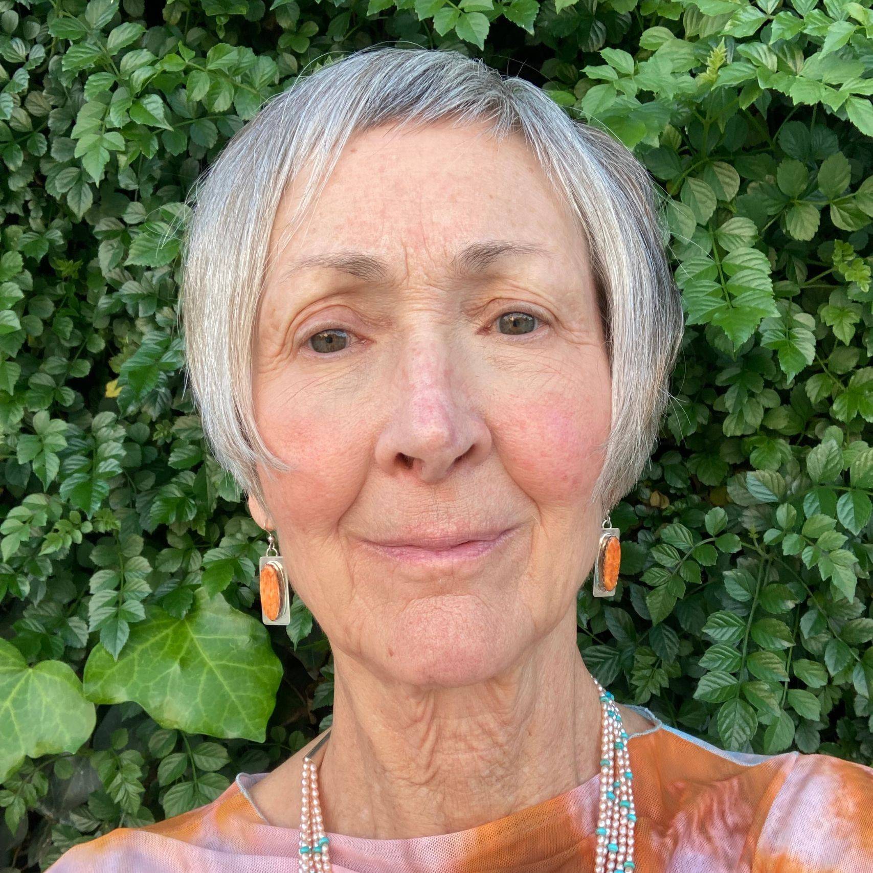 a person with grey hair and orange necklaces