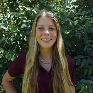 a person smiling in front of a bush