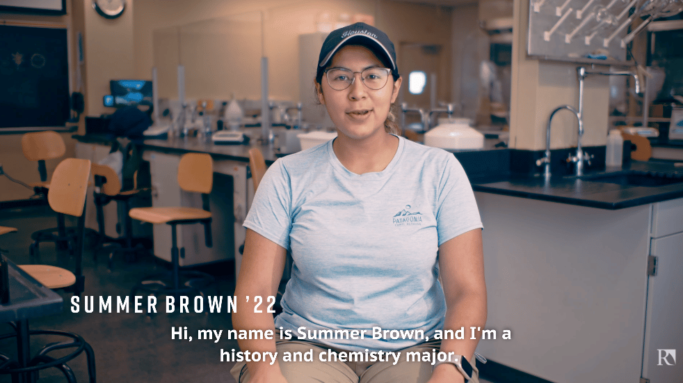 a person in a blue cap and glasses sitting in a room with a science lab