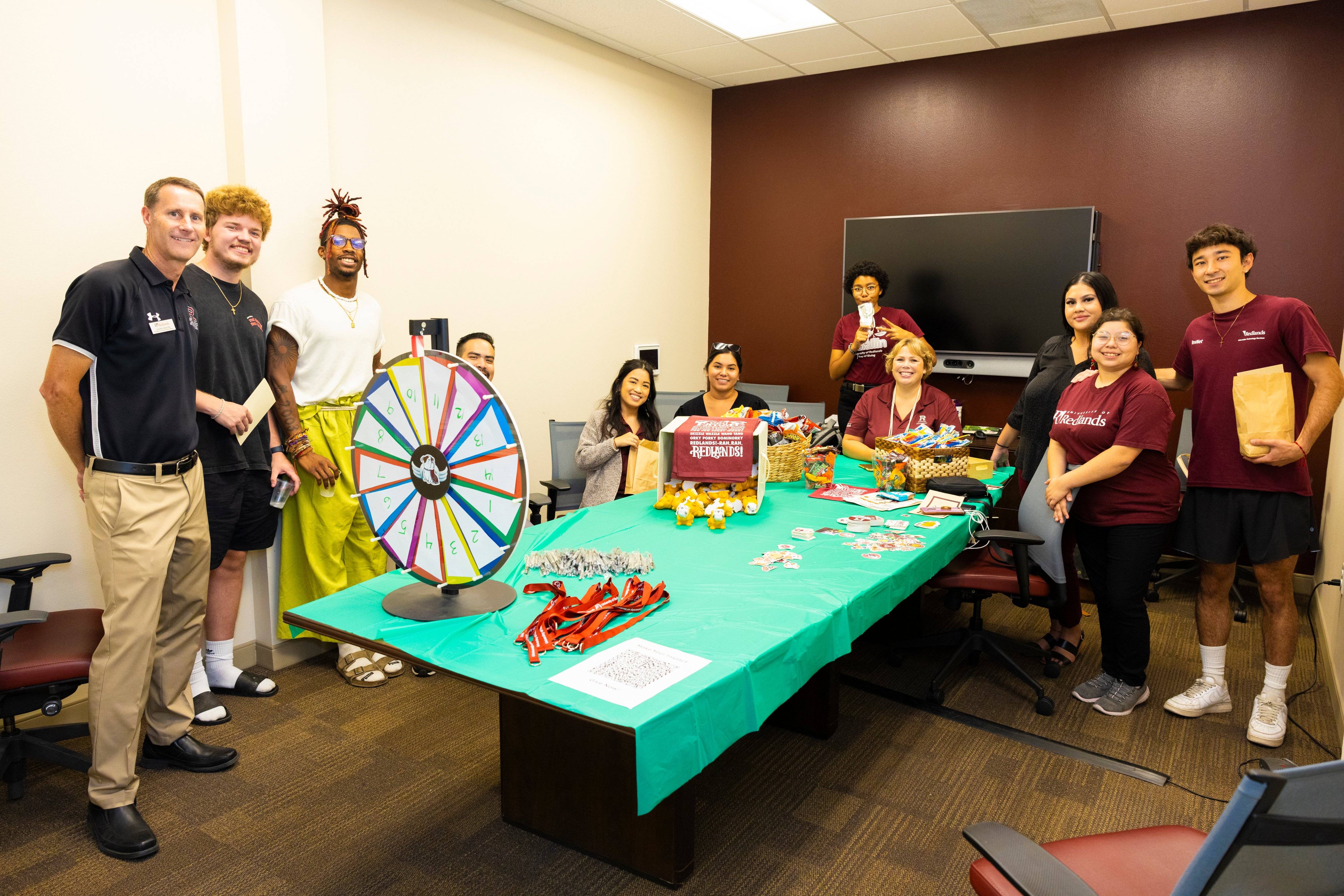 a group of people standing around a table with a table with candy and a wheel