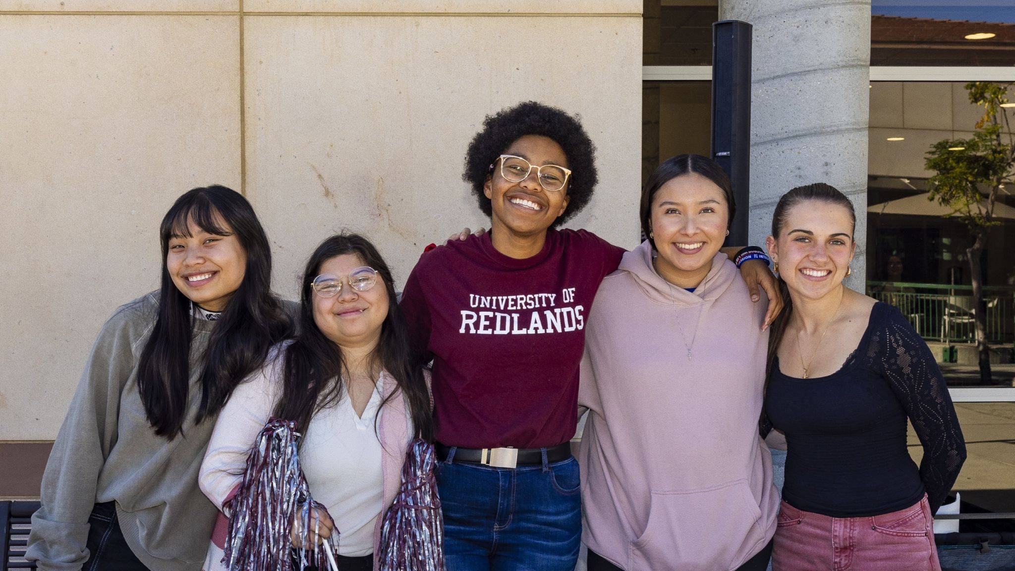 Five students standing together and smiling for a photo on campus.