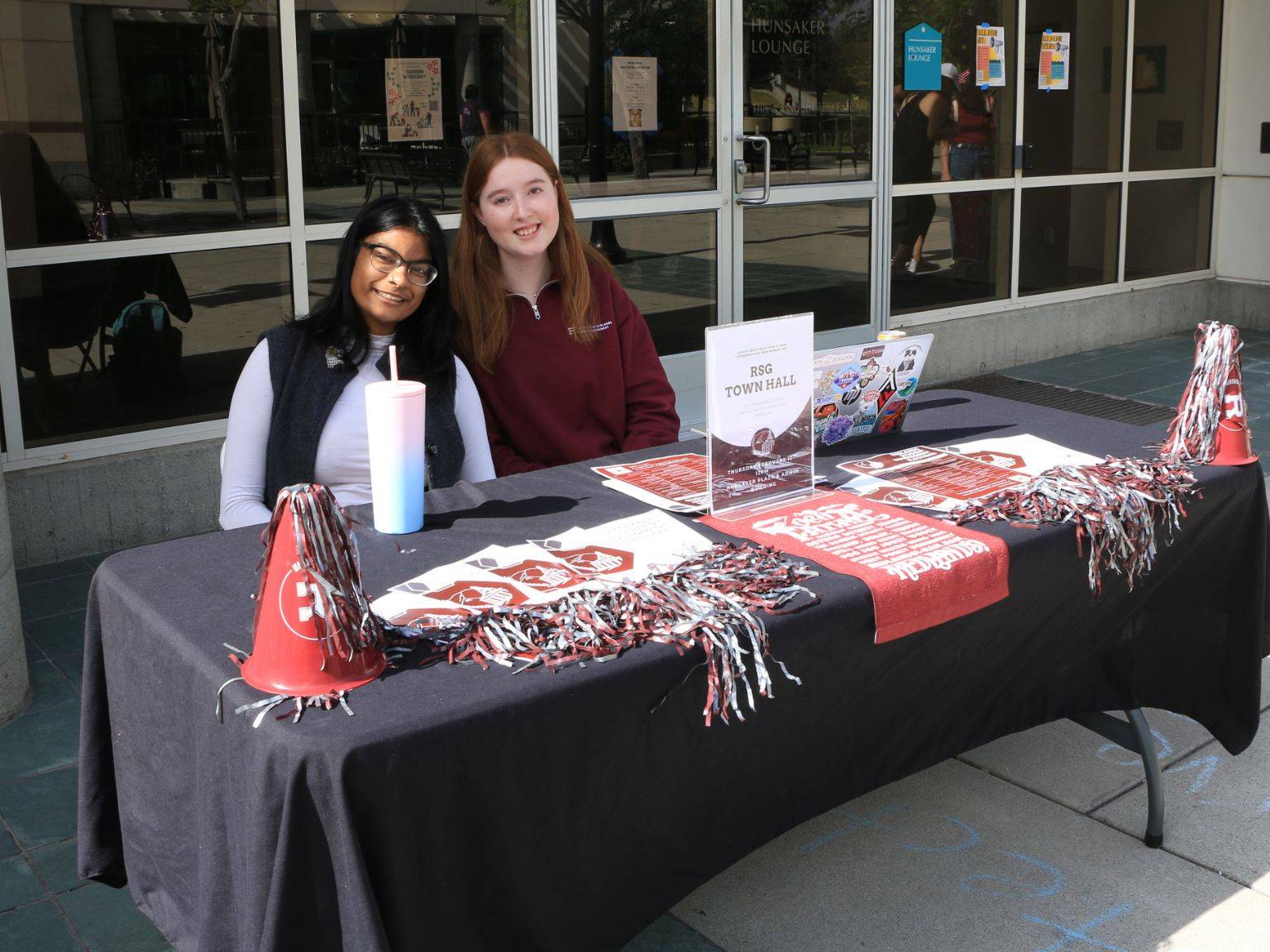 Two students smiling behind a table for Redlands Student Government on campus.