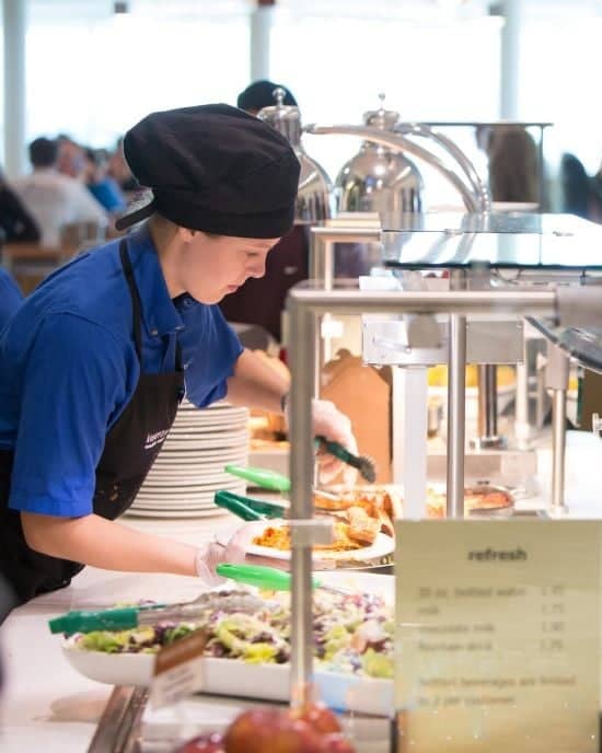A dining staff member prepares food behind a serving station in a dining hall on campus.