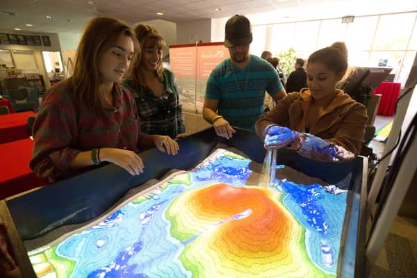 students gathering around projection of GIS map on tabletop sandbox